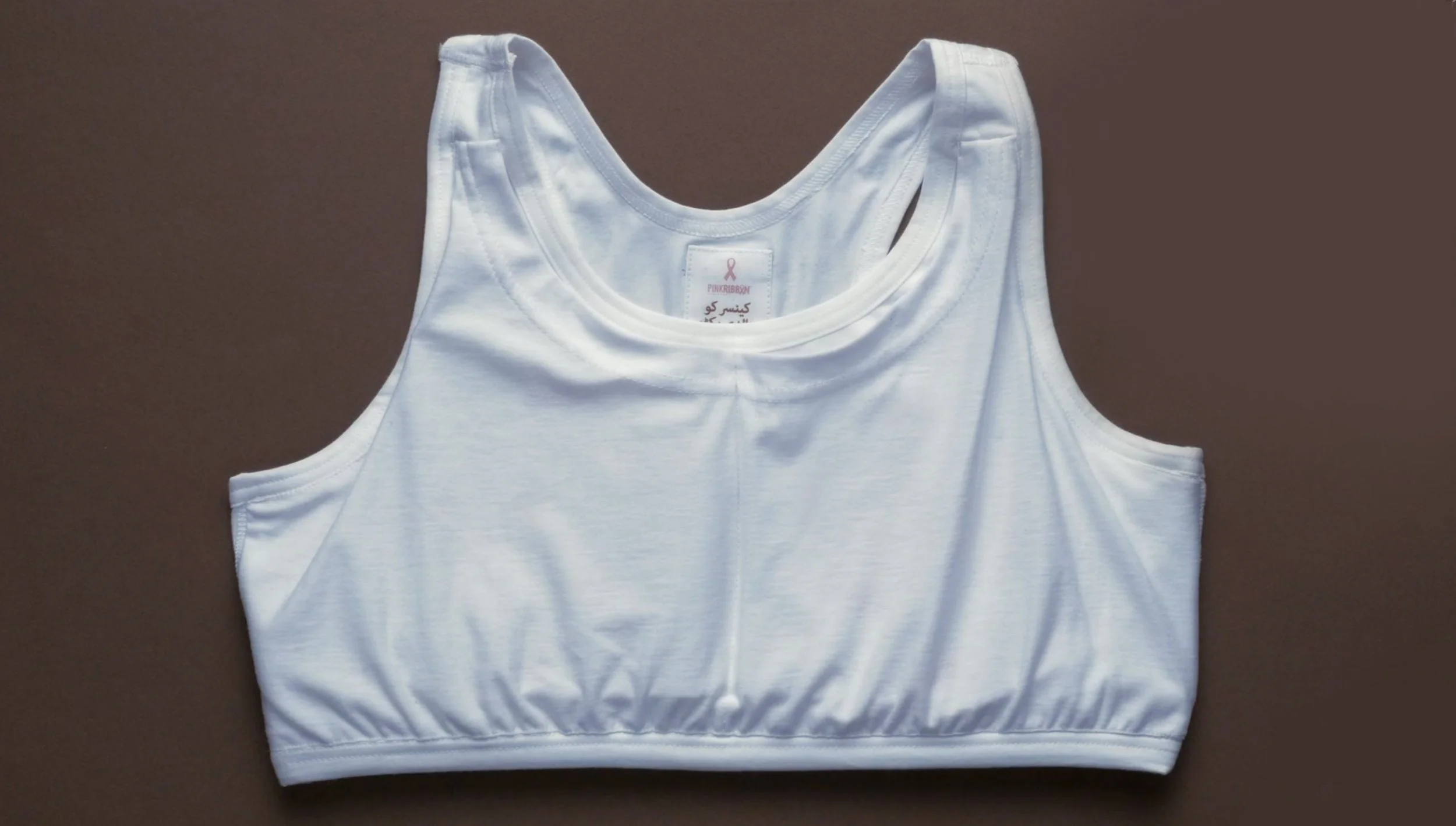 White sleeveless sports bra with pink ribbon logo and pink text on the inside.