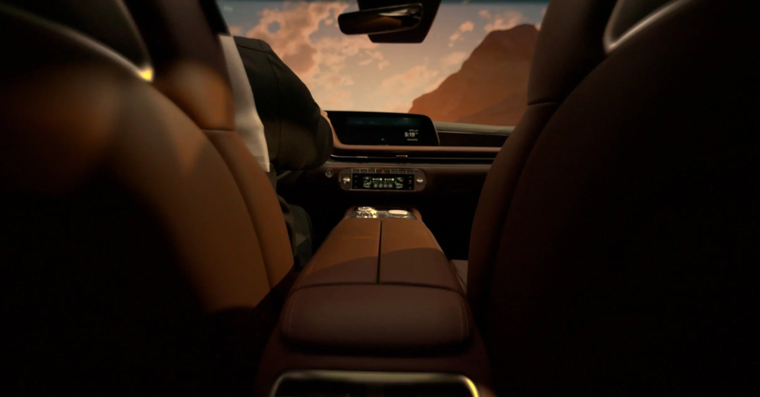 View from the back seat of a car showing the front seats, dashboard, and a sunset or sunrise scene with mountains through the windshield.
