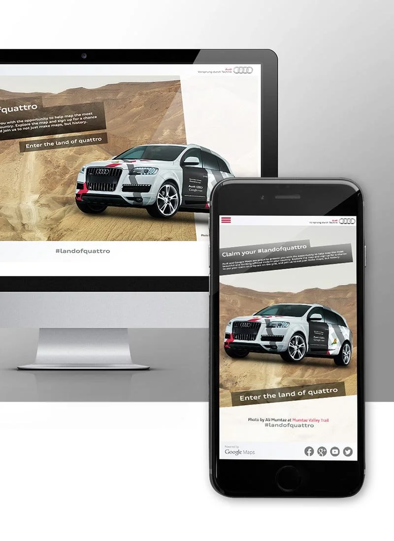 Responsive website displaying a digital rendering of an Audi SUV on a desert trail, with text promoting a 'land of quattro' campaign, shown on both a desktop monitor and a mobile phone.