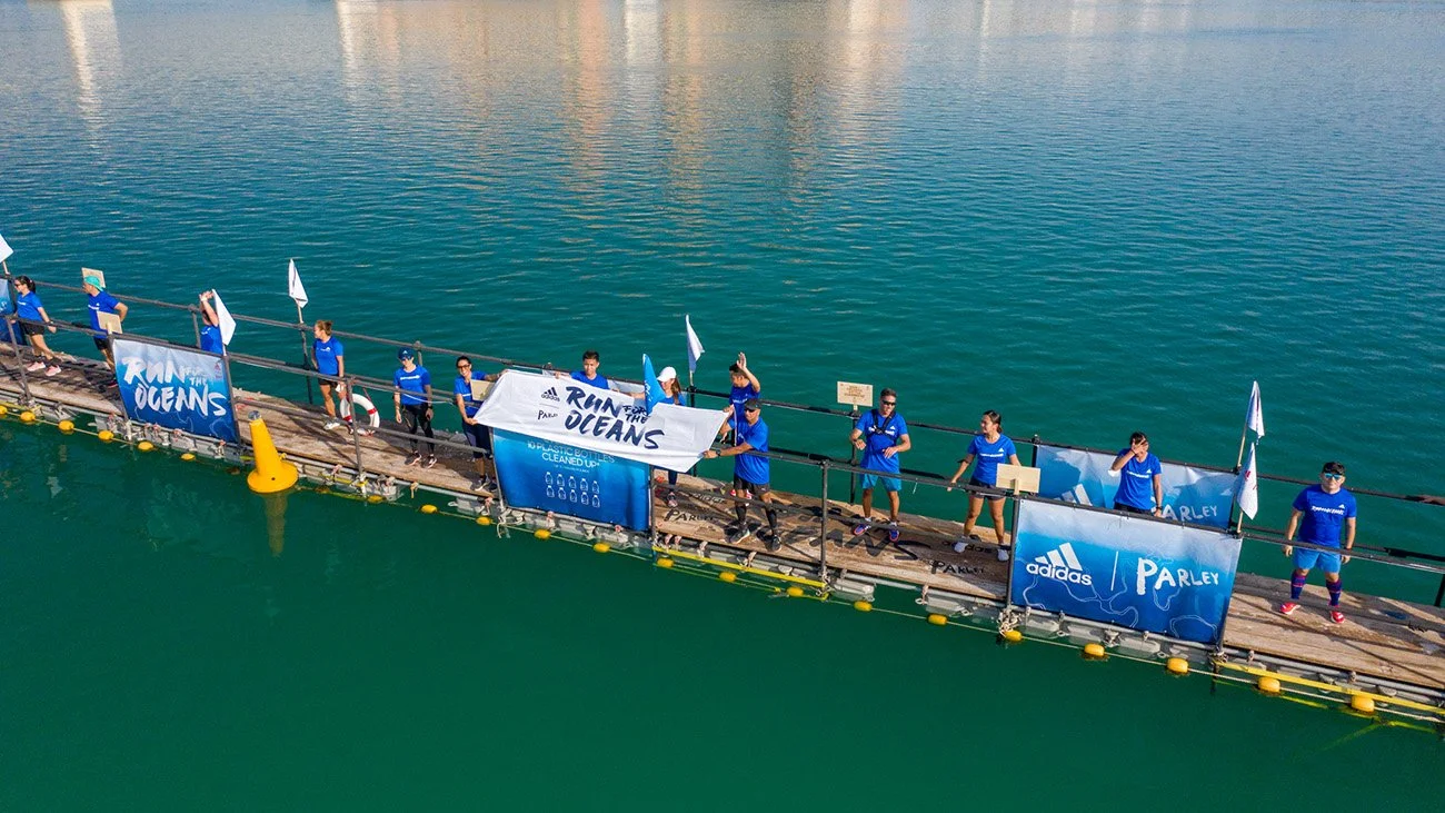 Group of people on a floating platform in the water, holding banners that say "Run for the Oceans" and standing in front of a large body of water.