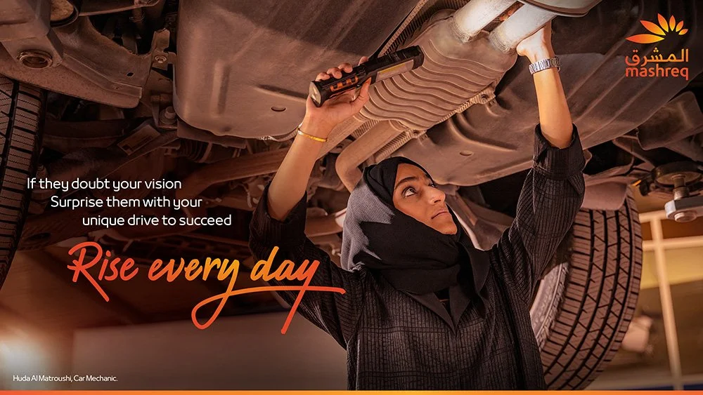 Woman mechanic inspecting and repairing the underside of a car using a flashlight in a garage or workshop.