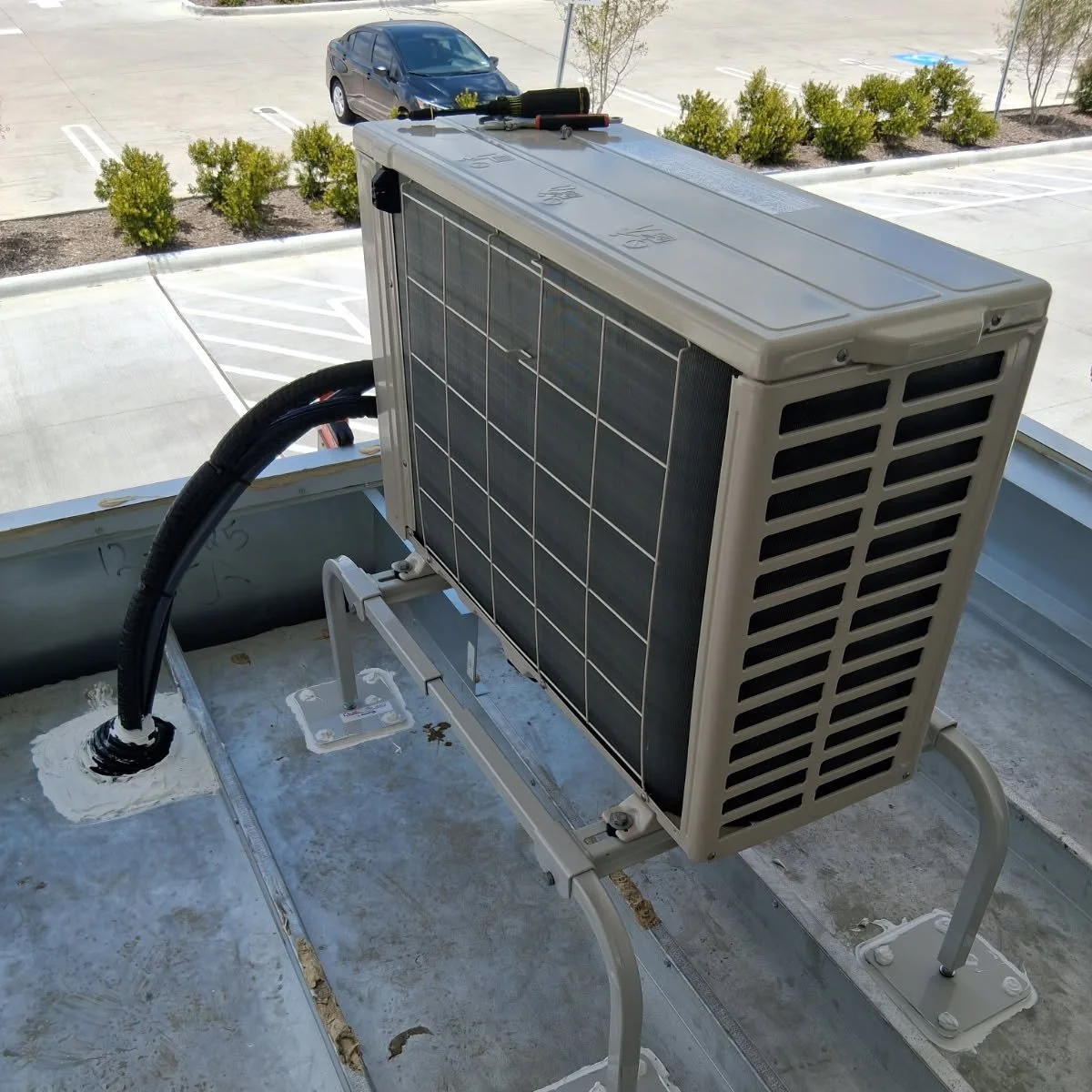 Air conditioning unit installed on the rooftop of a building with parking lot and trees in the background.
