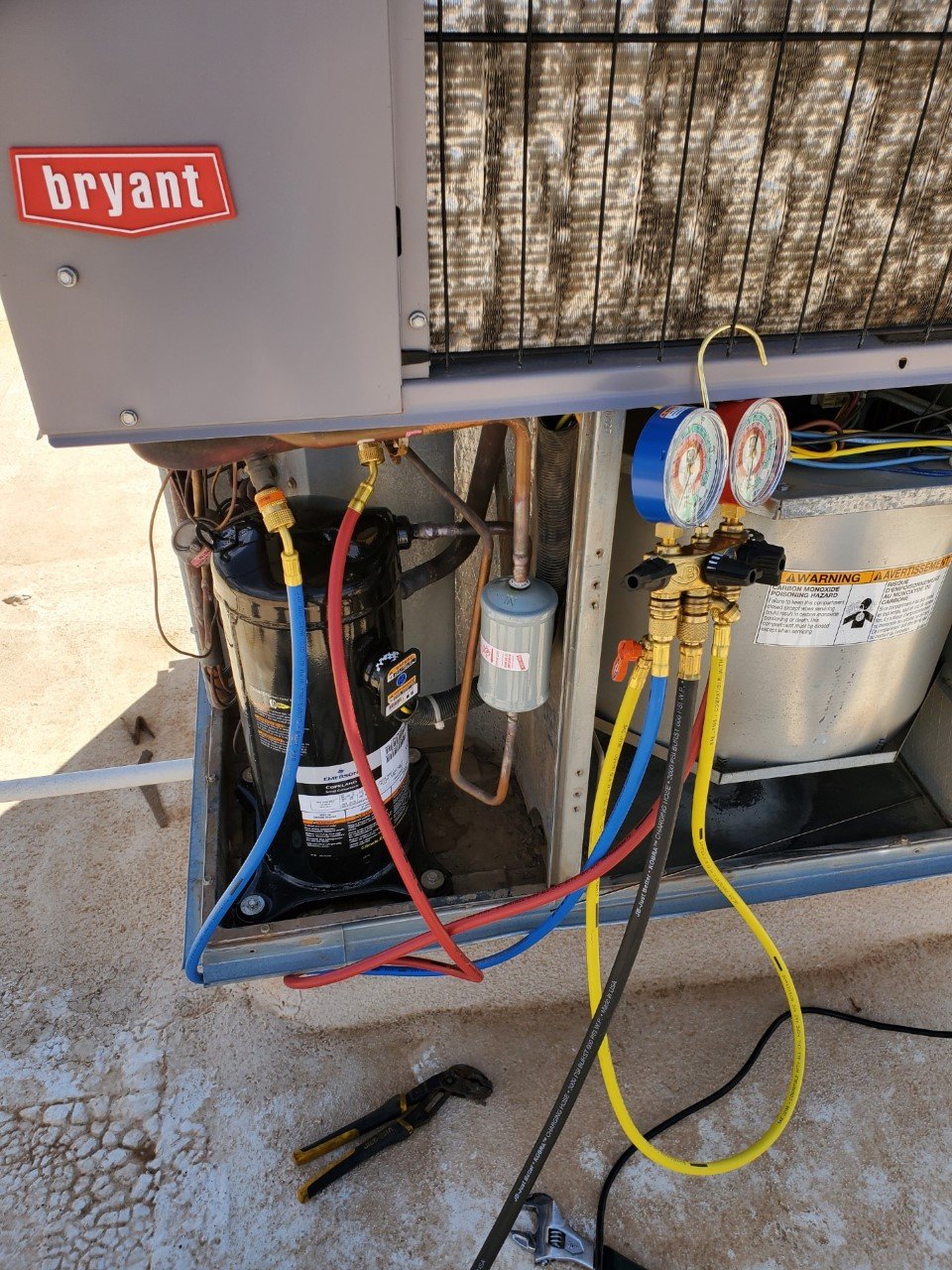 Open HVAC unit with tools, gauges, refrigerant lines, and internal components visible.