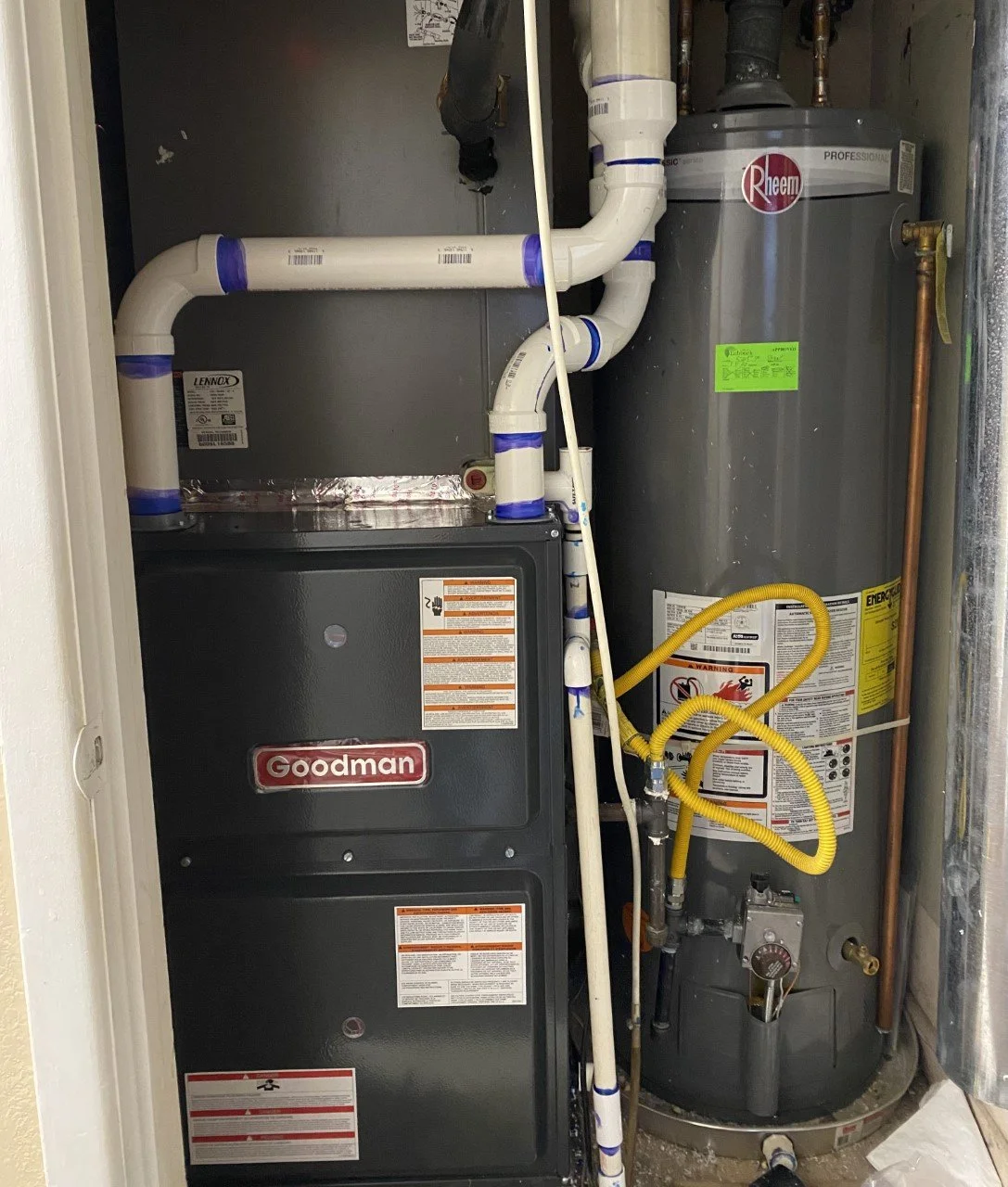 Furnace and water heater unit with pipes, gauges, and labels in a utility closet.