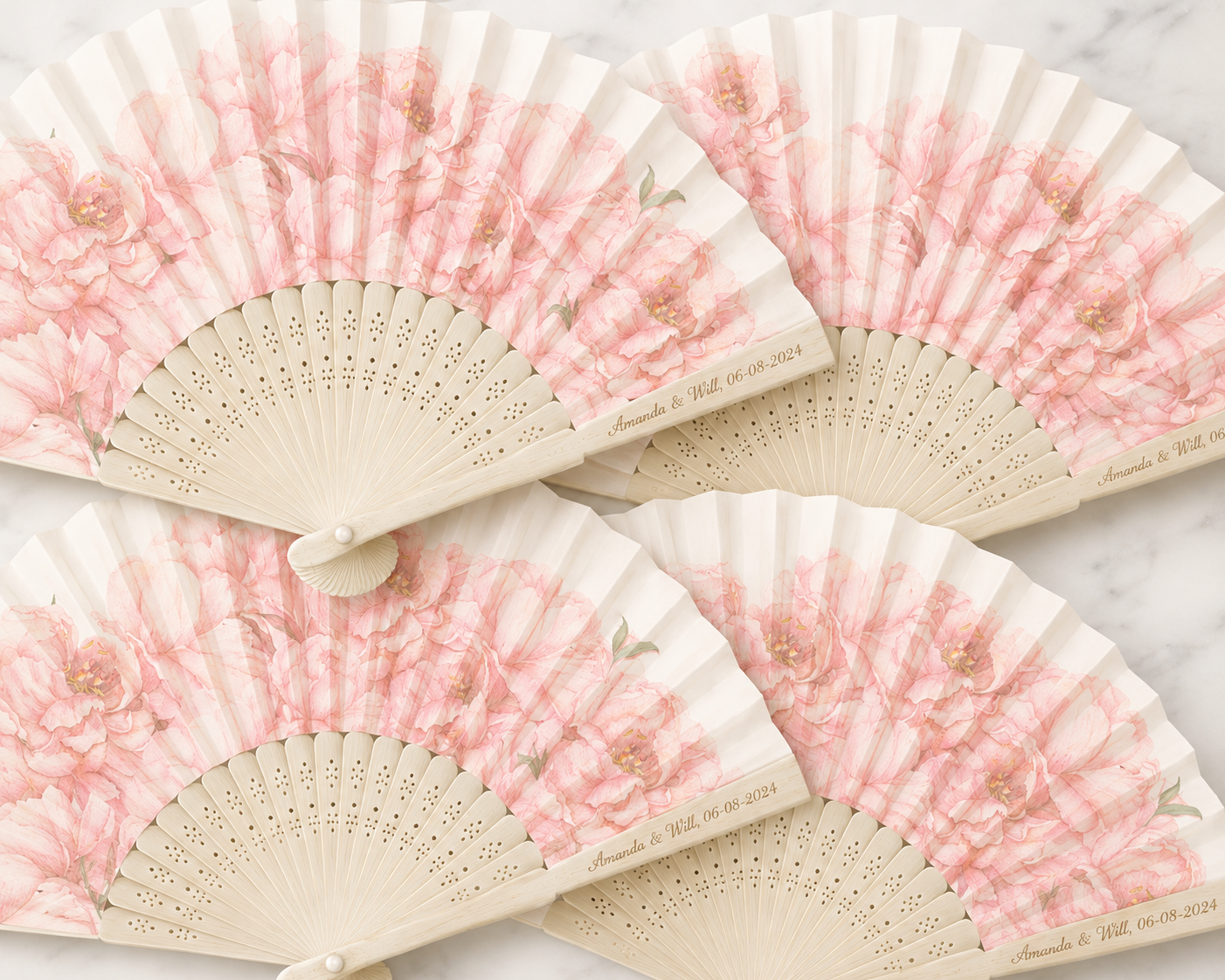 Four decorative handheld fans with pink floral patterns and personalized text, placed on a white marble surface.