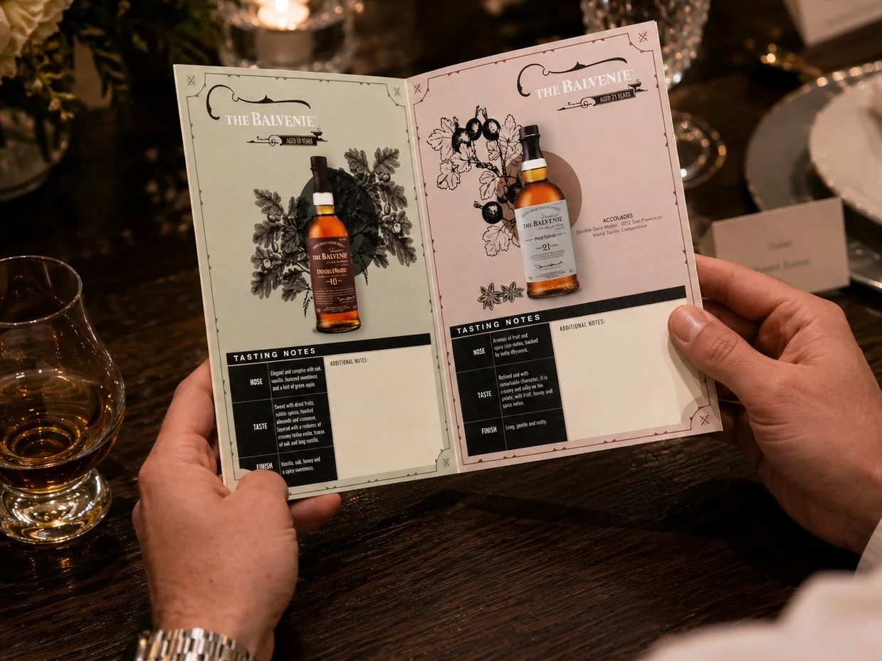 Interior spread of a custom scotch tasting booklet designed for The Balvenie, featuring antique botanical illustration, tasting notes, and structured layout for the DoubleWood 10 Year and 21 Year expressions, photographed being held open at a candlel