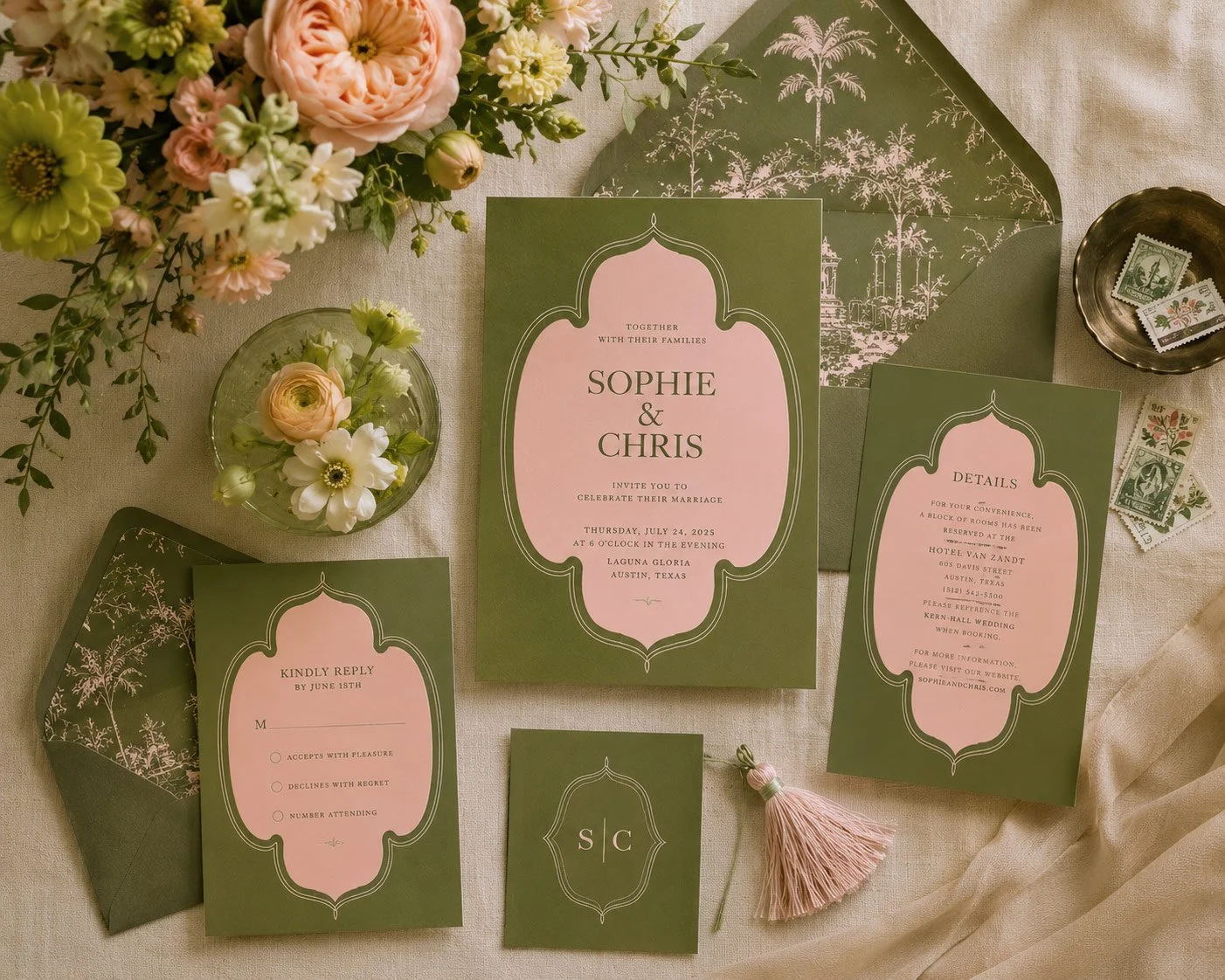 Wedding invitation set with green and pink color scheme, featuring floral details, RSVP card, and ceremony details, surrounded by flowers, a tassel, and vintage stamps on a cream fabric background.