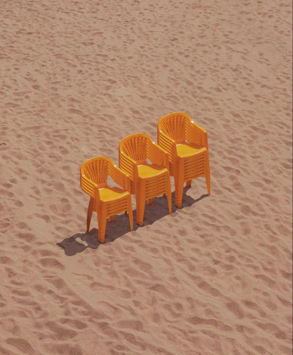 Trois chaises en plastique orange empilées sur du sable au bord de la plage. Santa Brevina