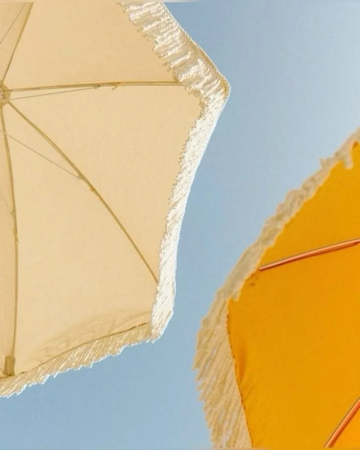 Deux parasols, un beige et un jaune, vus de dessous contre un ciel bleu clair. Santa Brevina