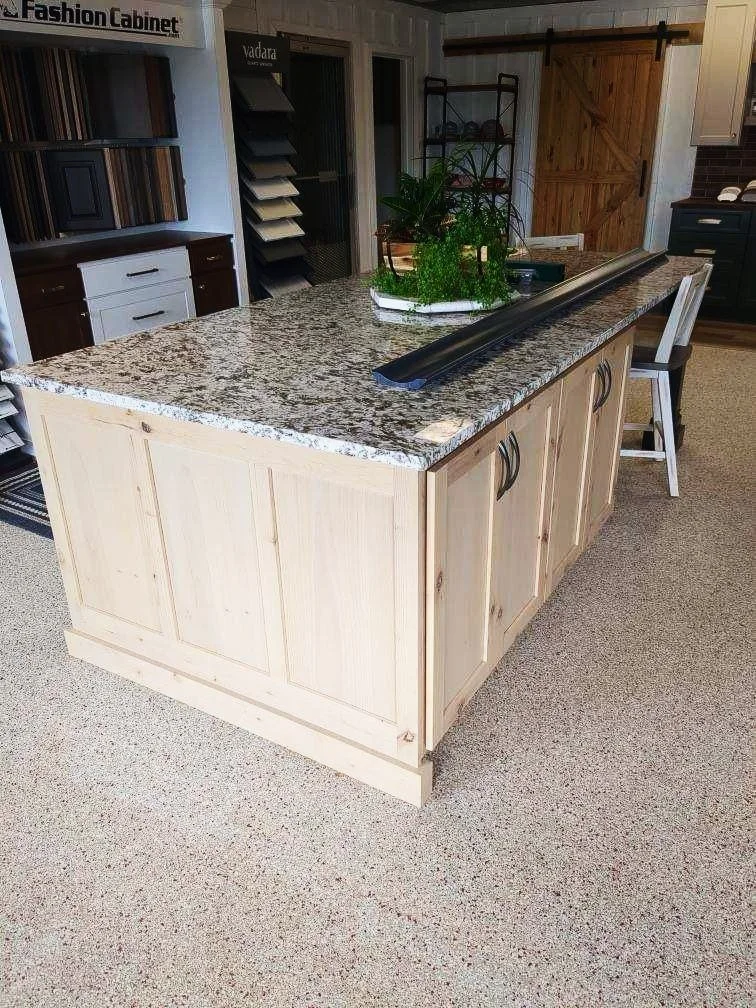 Kitchen island with a granite countertop, wooden base, and black handles, with a chair nearby, plants and decorative items on top, and a barn-style sliding door in the background.