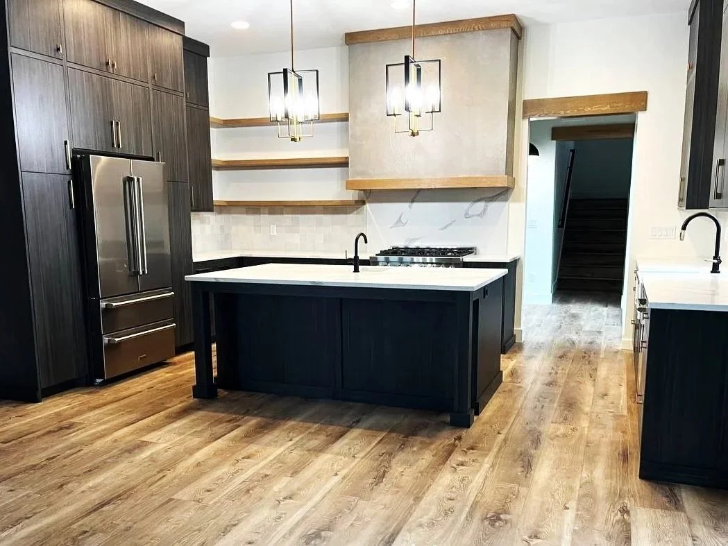 Modern kitchen with dark cabinets, a central island, wooden floors, open shelving, and pendant lighting.