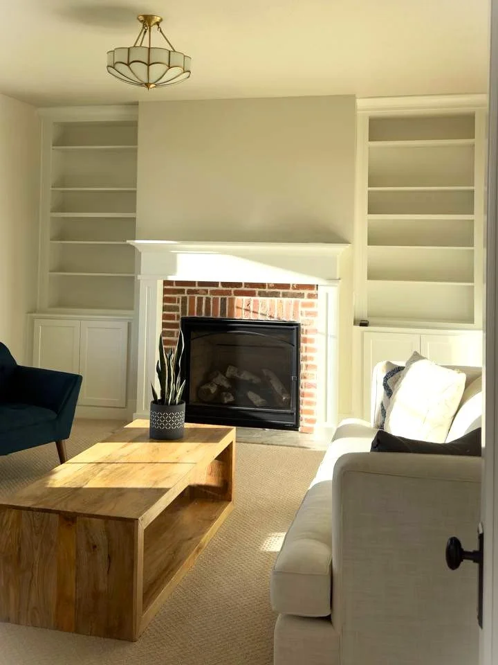 Living room with a fireplace, white built-in shelves on each side, a beige couch, a wooden coffee table, a potted plant, and a ceiling light fixture.