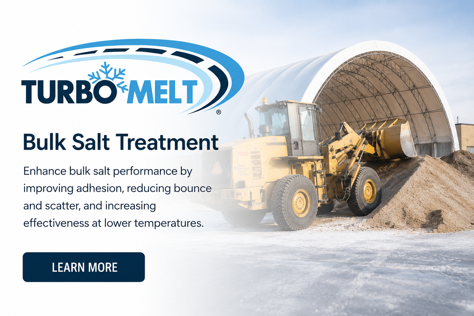 A large yellow bulldozer spreading bulk salt in front of a white covered storage building, with a snow-covered ground and a blue sky.