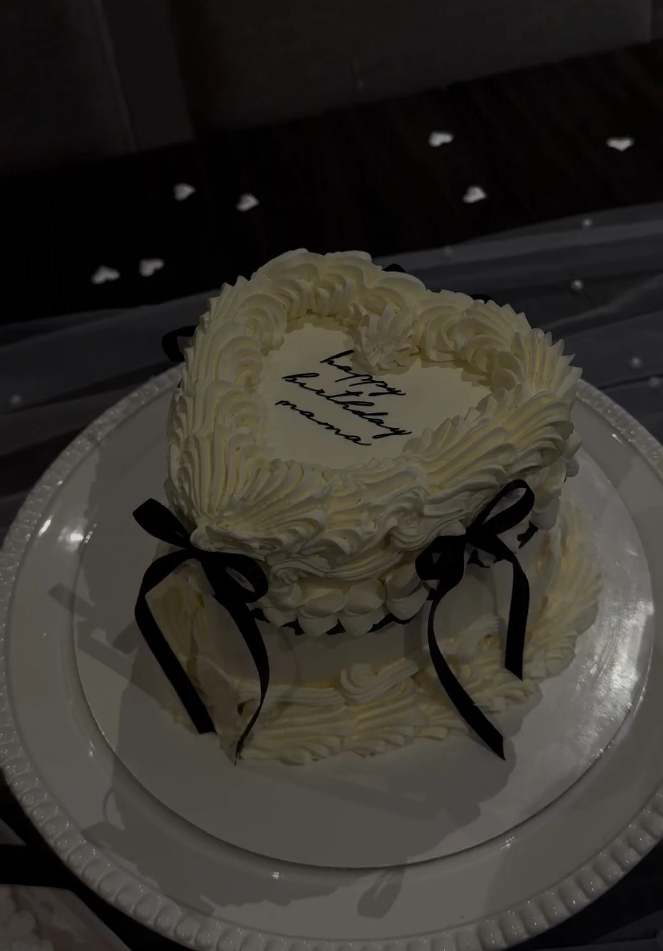 Round birthday cake with white frosting and black ribbon decorations on a silver tray, with the words 'happy birthday mama' written on top.