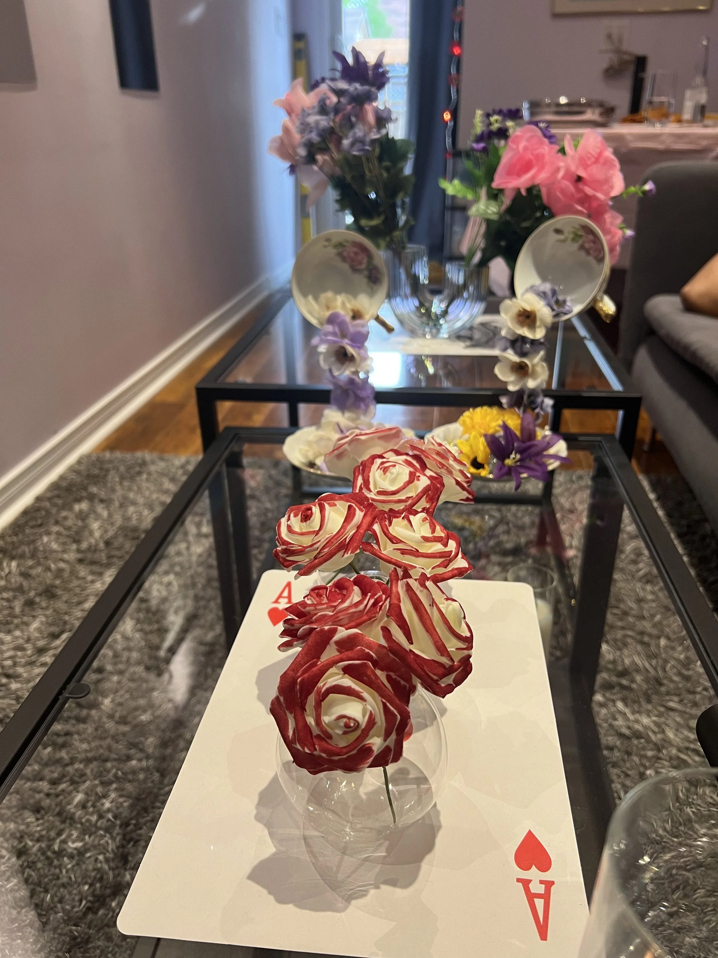 A glass of shaved ice dessert decorated with red and white swirled design resembling roses, placed on a white surface with an Ace of Hearts playing card partially visible underneath.