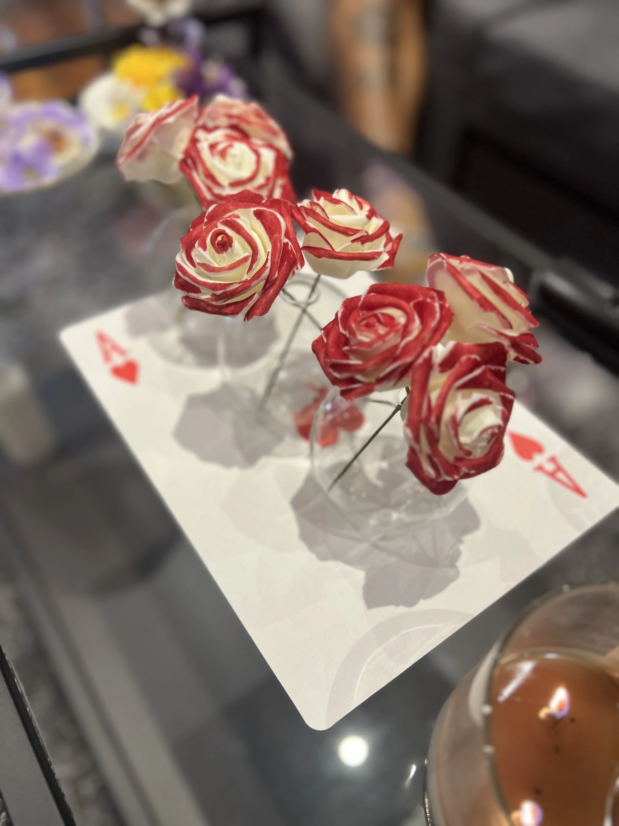 Close-up of handmade red and white roses on a display stand, with additional flowers blurred in the background.