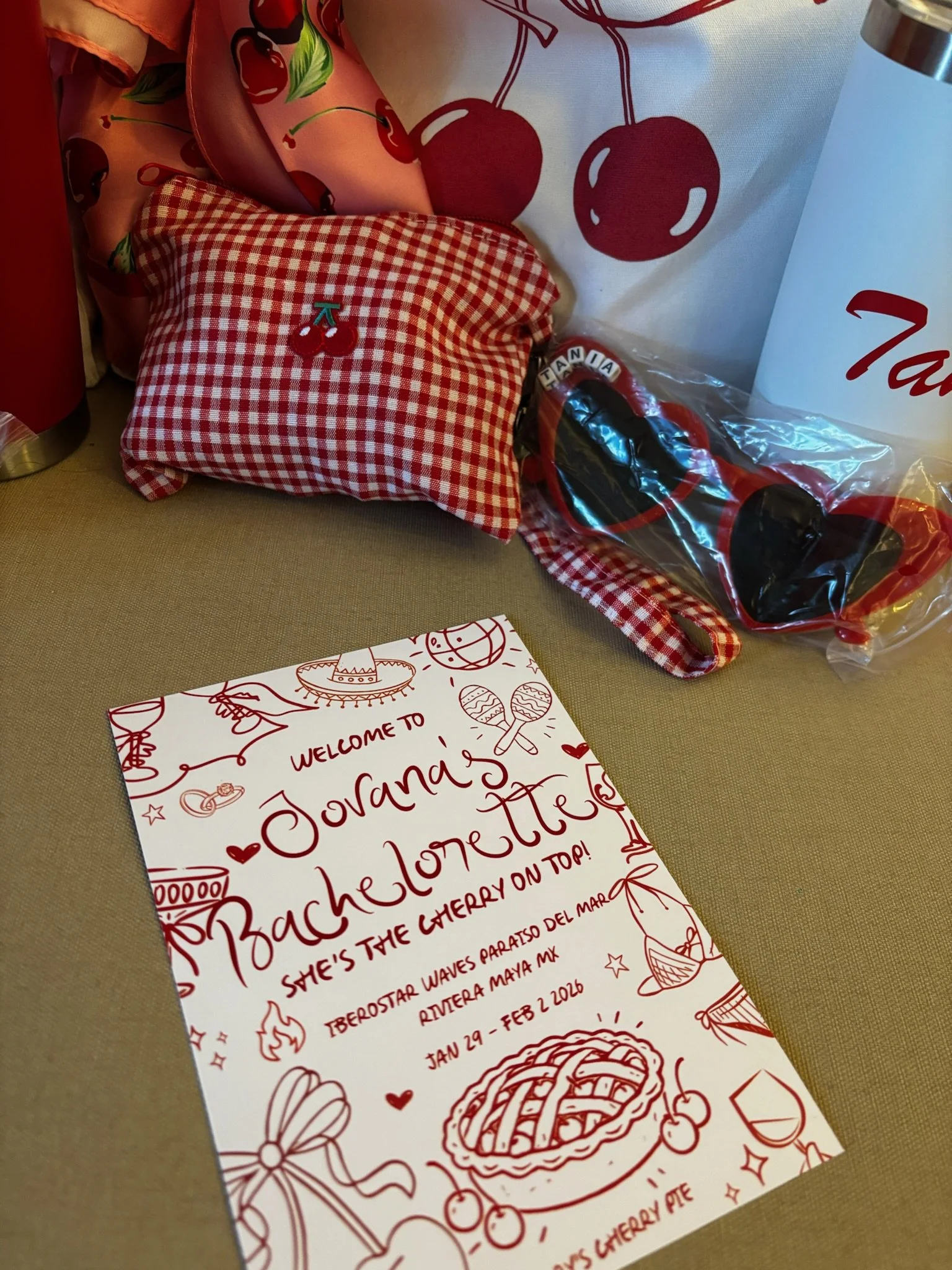 A decorative table setting with a red and white checkered cloth pillow featuring a cherry embroidery, a red and black pie-shaped pie tin with the words "Thank You" written in beads, a white cup with a red Cherry themed design, and a handmade banquet 