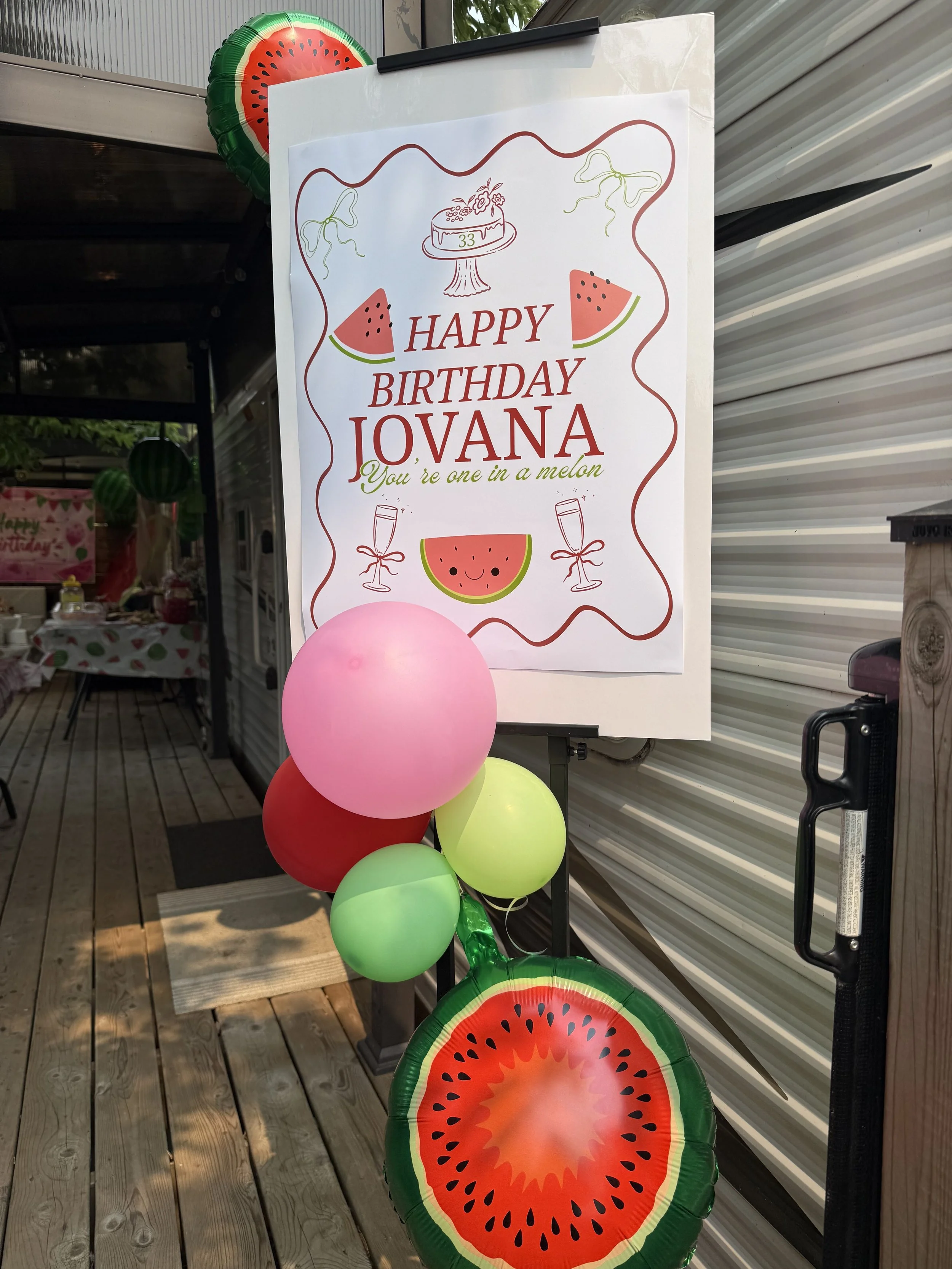 A birthday decoration with a sign saying "Happy Birthday Jovana" surrounded by watermelon-themed balloons and a watermelon slice paper cutout.
