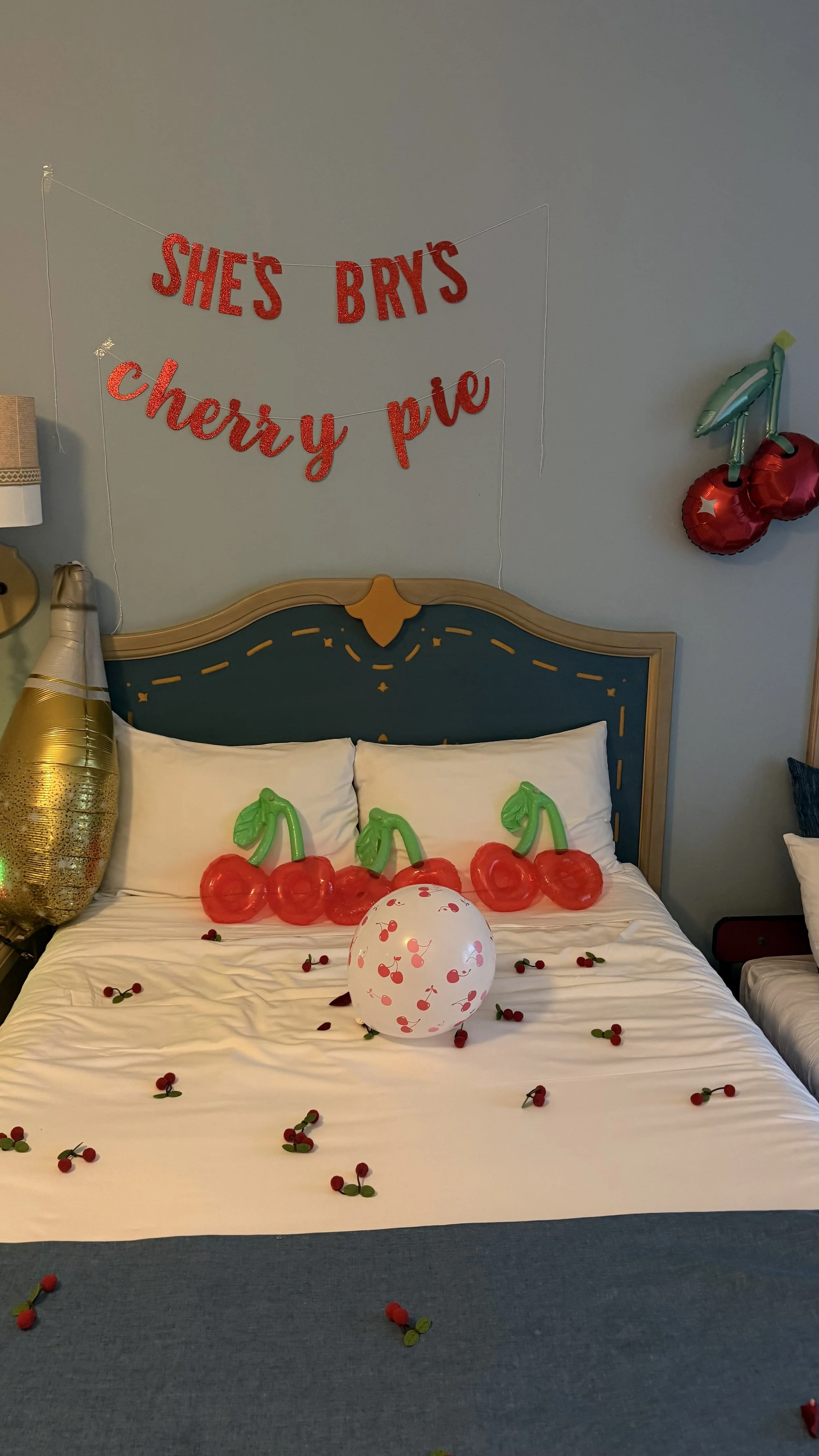 Decorated bed with cherry-themed balloons and scattered cherry decorations, with a cherry pie sign and cherry-shaped balloons on the wall, celebrating a birthday or special occasion.