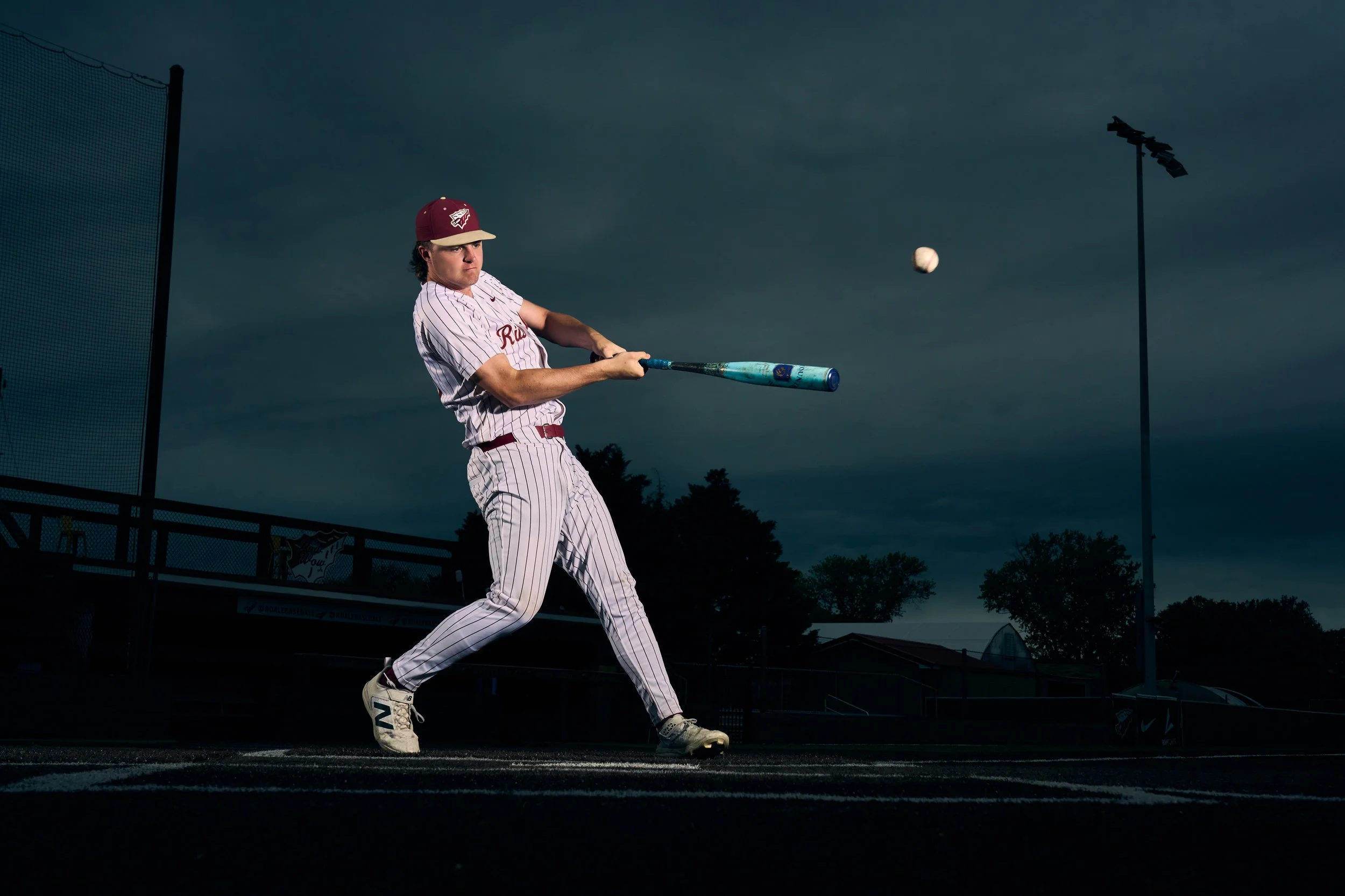 A baseball player in a uniform and cap attempting to hit a pitched ball with a bat during a game at dusk.