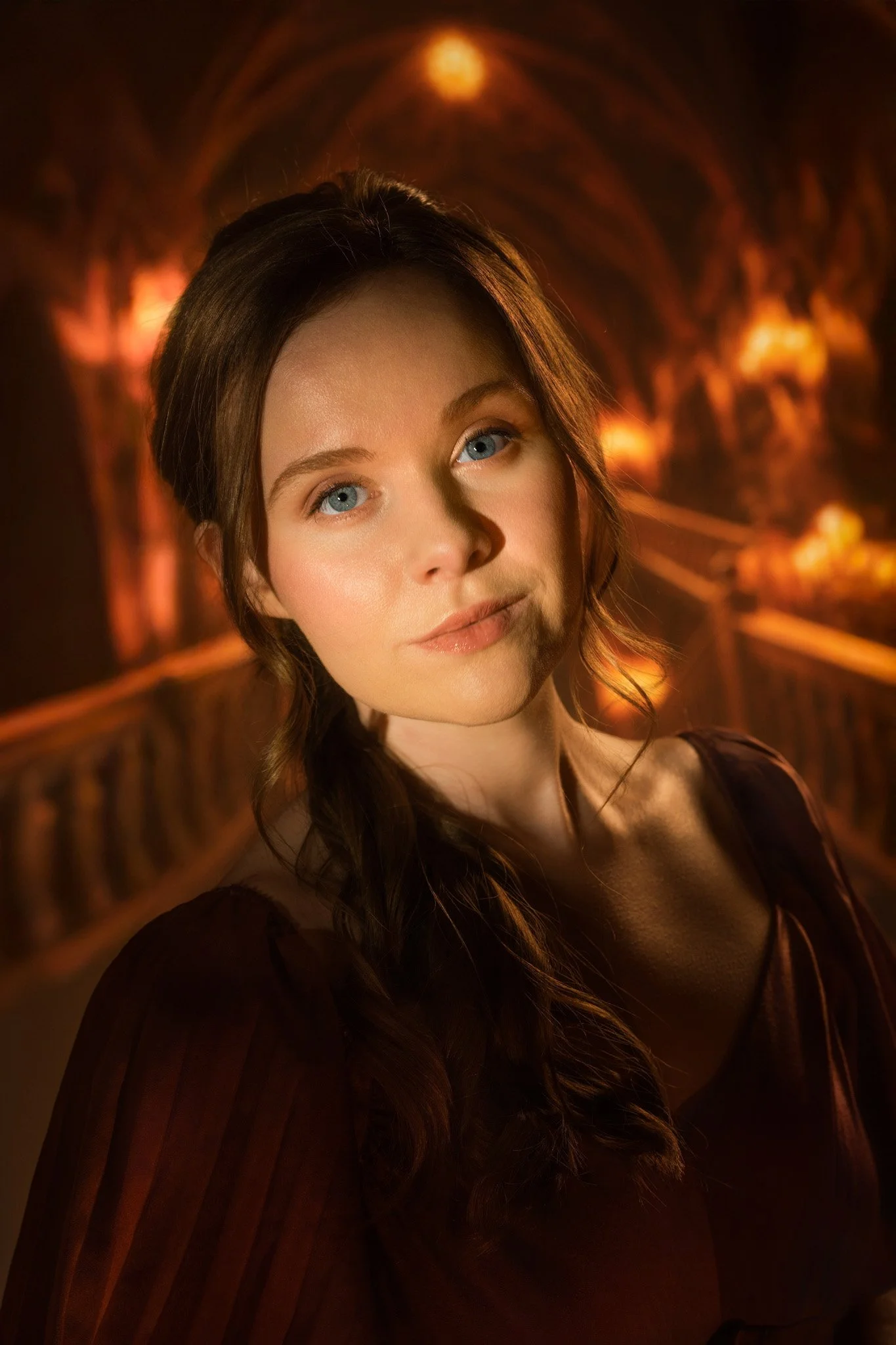 A woman with long brown hair and blue eyes looking slightly away with a blurred, warm-toned background.
