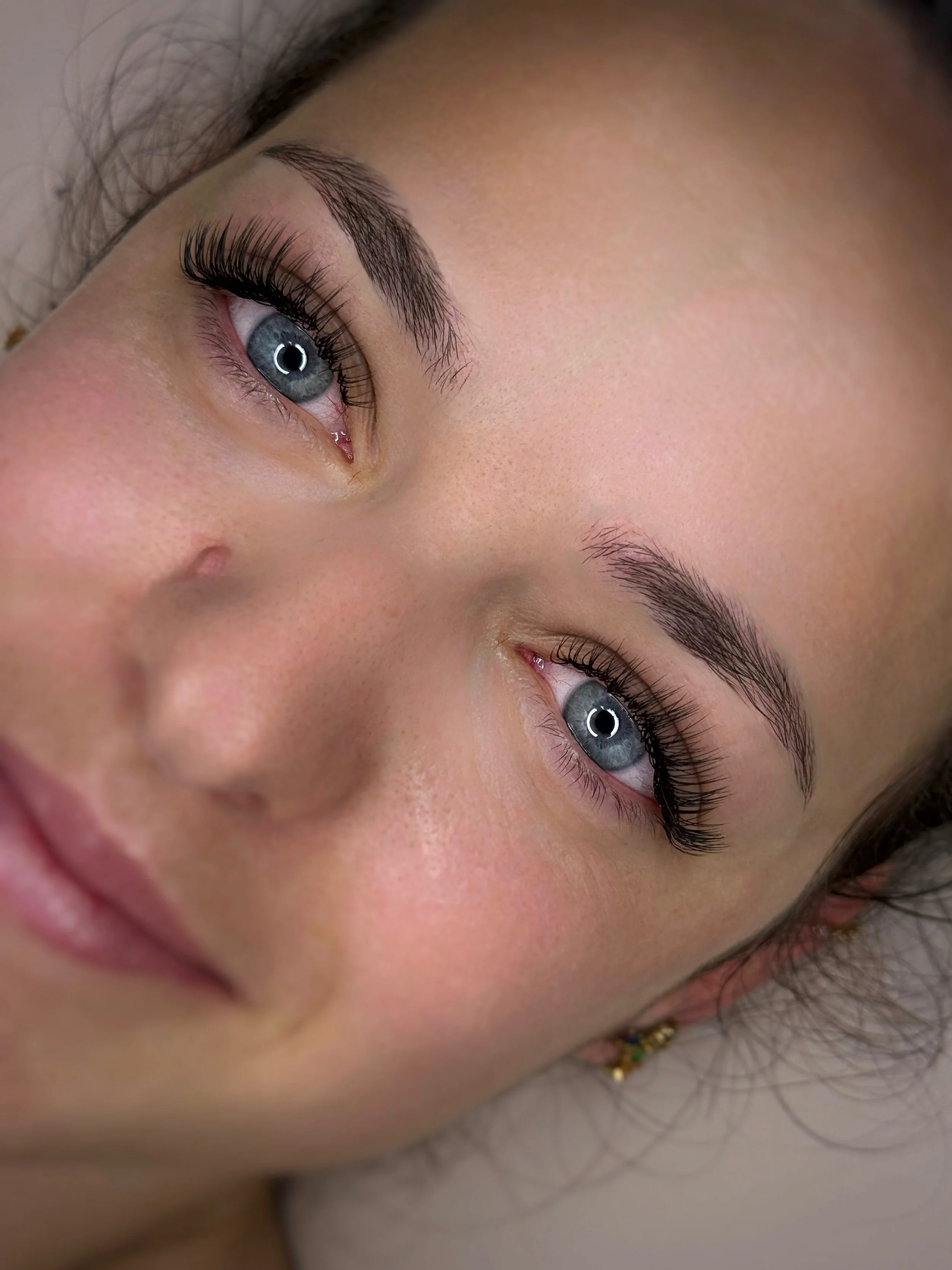 Gros plan d'un visage féminin, mettant en évidence des yeux bleus avec des cils longs et un maquillage subtil, ainsi que des sourcils bien dessinés.