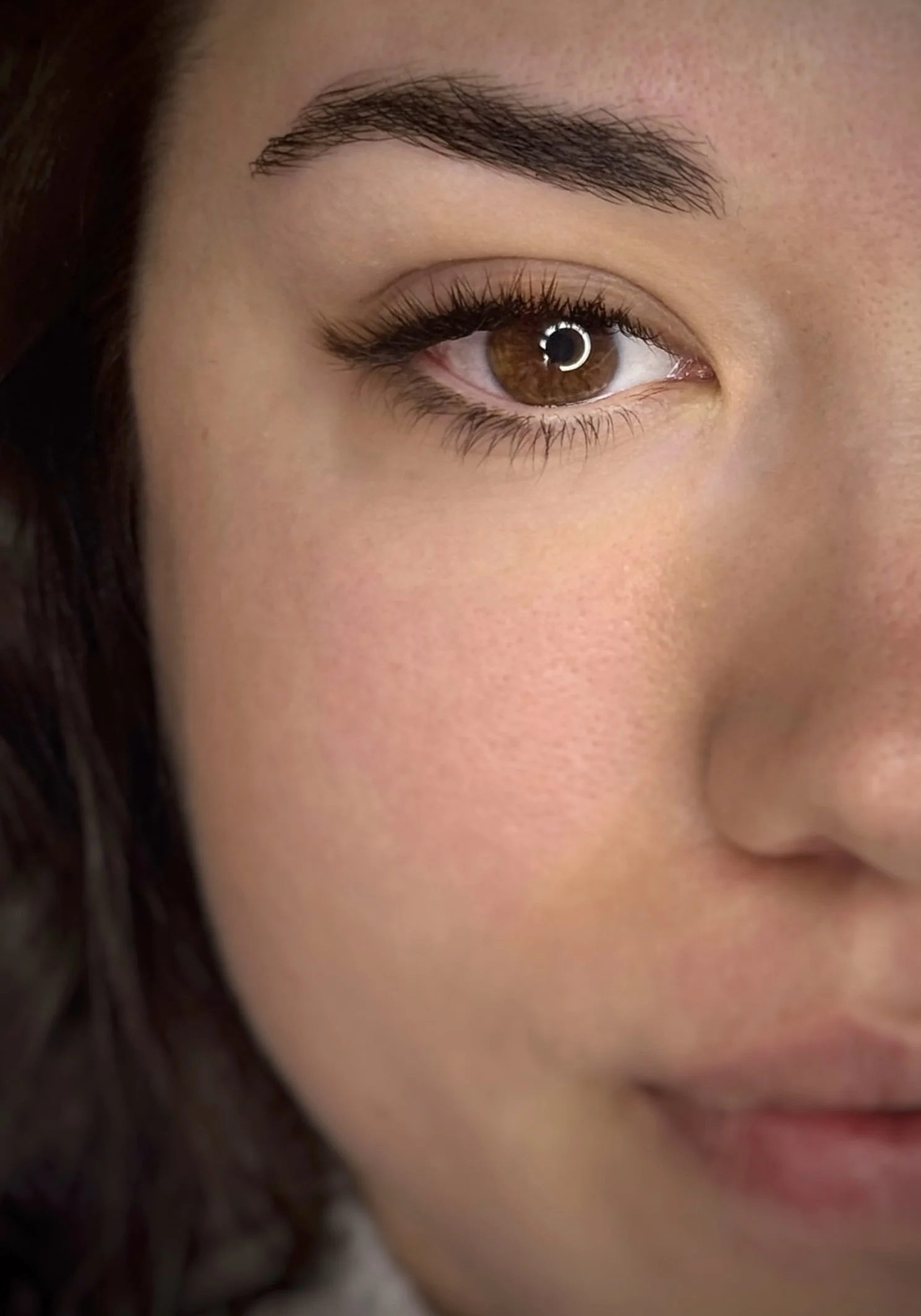 Gros plan d'un visage de femme, mettant en valeur un œil brun et le sourcil. La peau est lisse et naturelle.