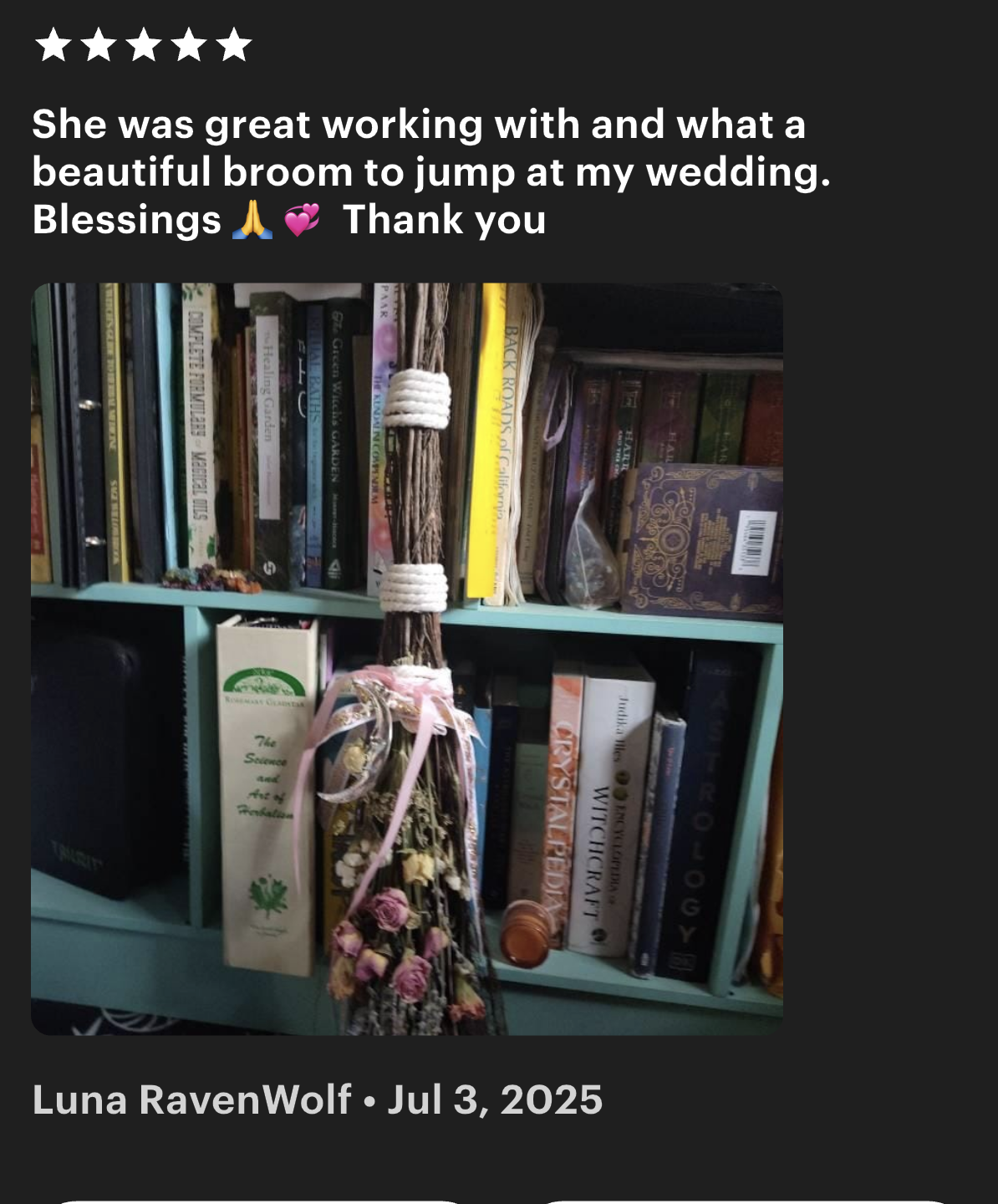 A small bookshelf with a bunch of books and a broom decorated with flowers and ribbons hanging from it.