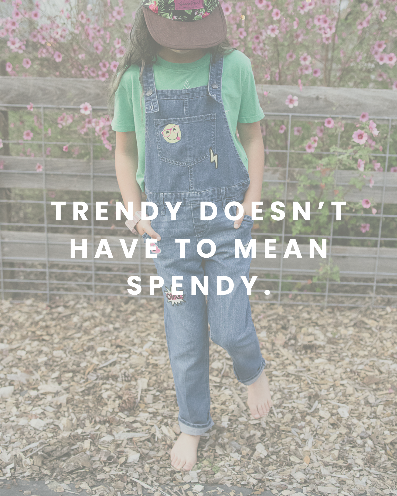 Child wearing a green T-shirt, denim overalls with patches, and a cap, standing outside in front of a fence with pink flowers, with the quote "Trendy doesn’t have to mean spendy" overlaid for Hand It Down Kid to Kid Resale Shop in Santa Cruz, CA.