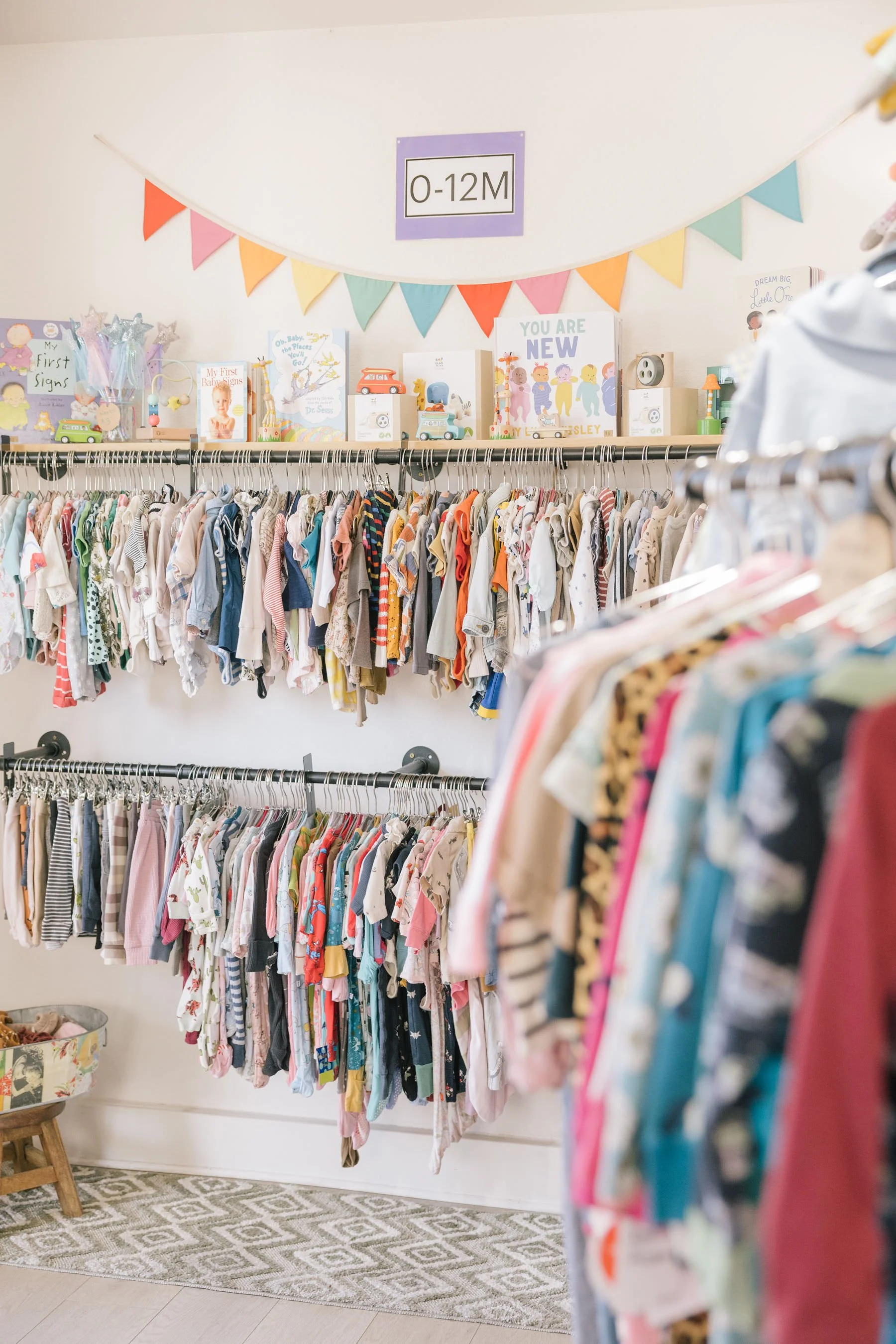 Clothing display for infants ages 0-12 months with a colorful banner above.