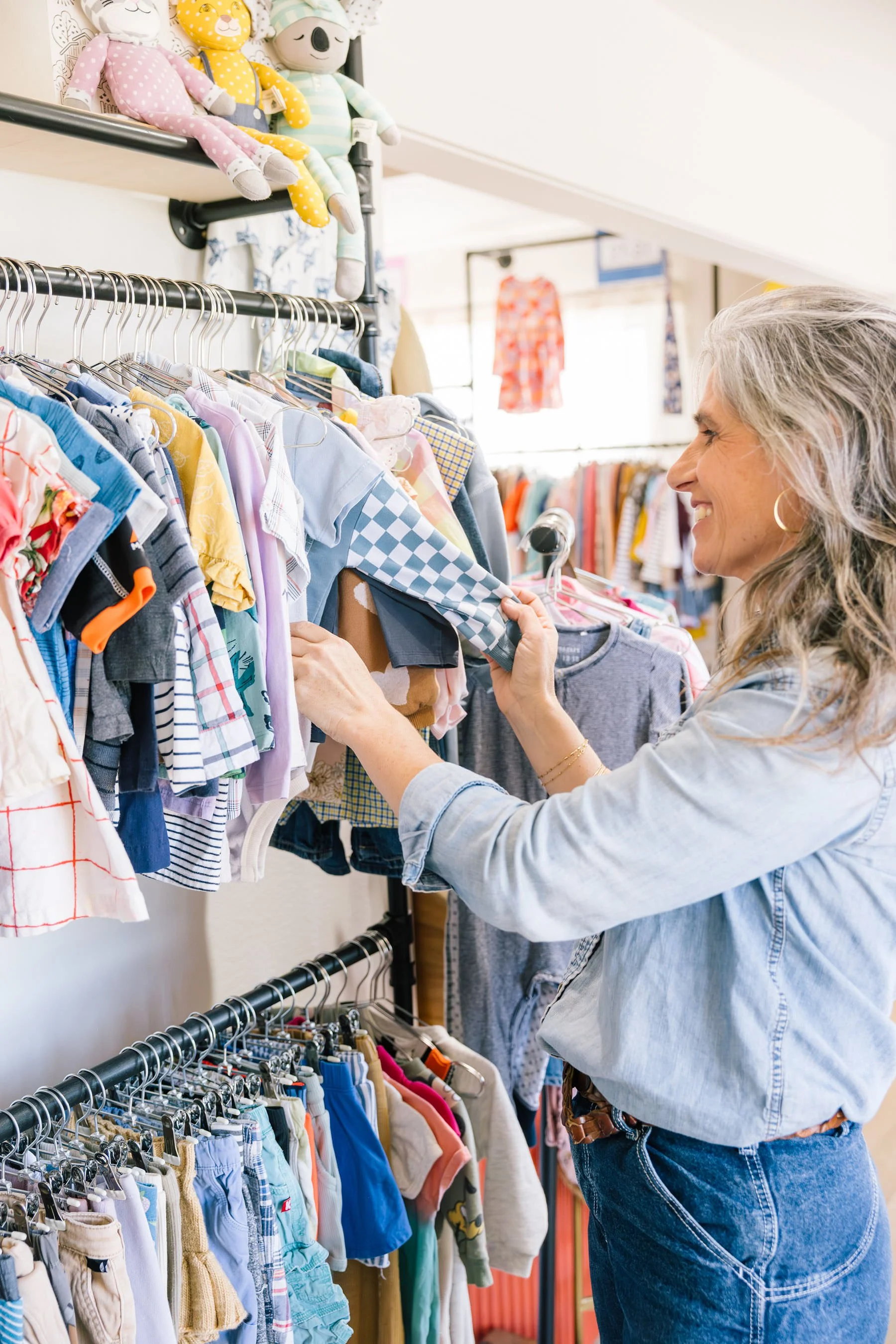 Tori Koneya, owner of Hand It Down Kid to Kid Resale Shop in Santa Cruz, CA browsing children's clothes at her store full of colorful shirts and pants on racks.