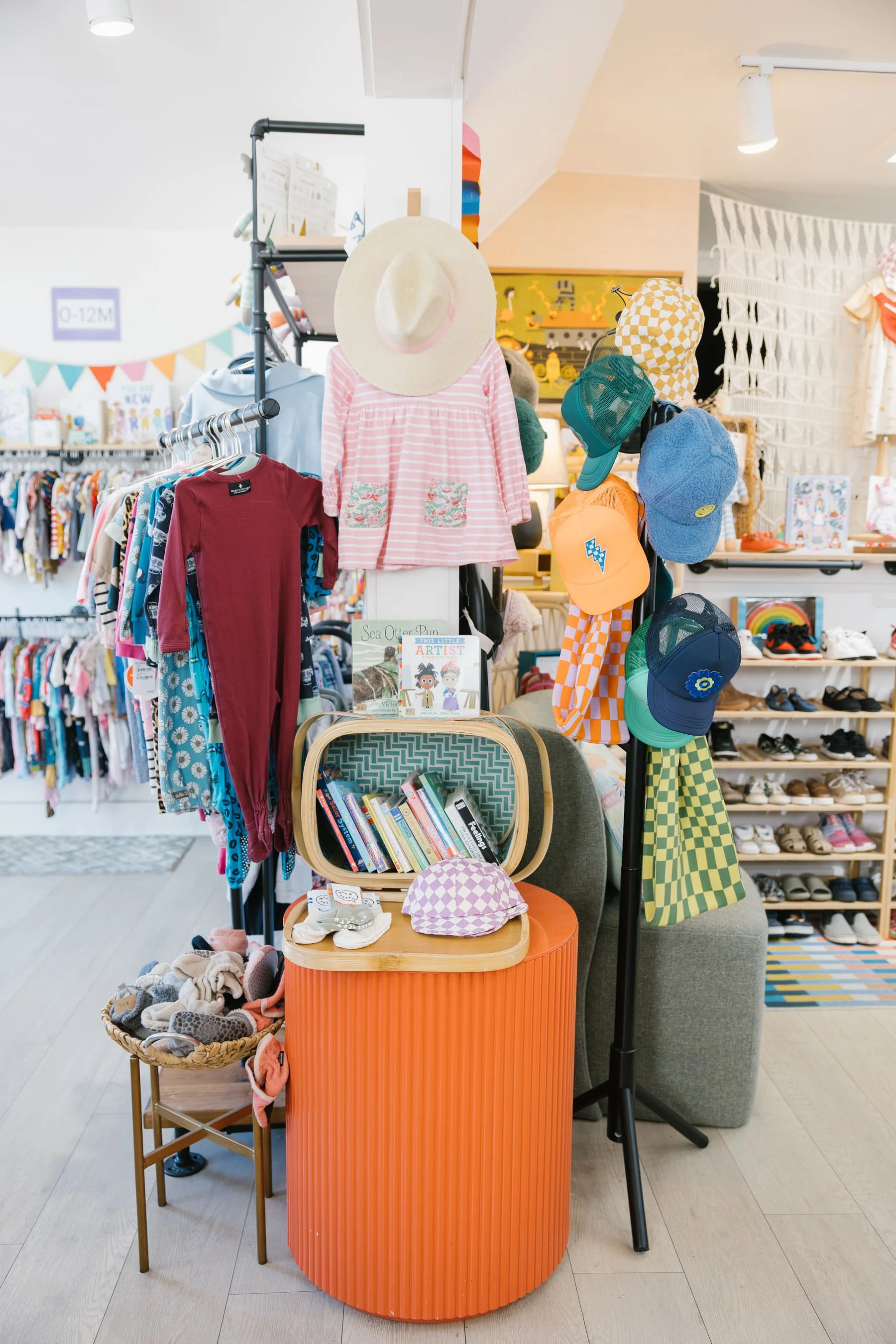 Display of children's clothing and accessories in a retail store, including hats, caps, and shirts with various patterns and colors, set on racks and shelves.