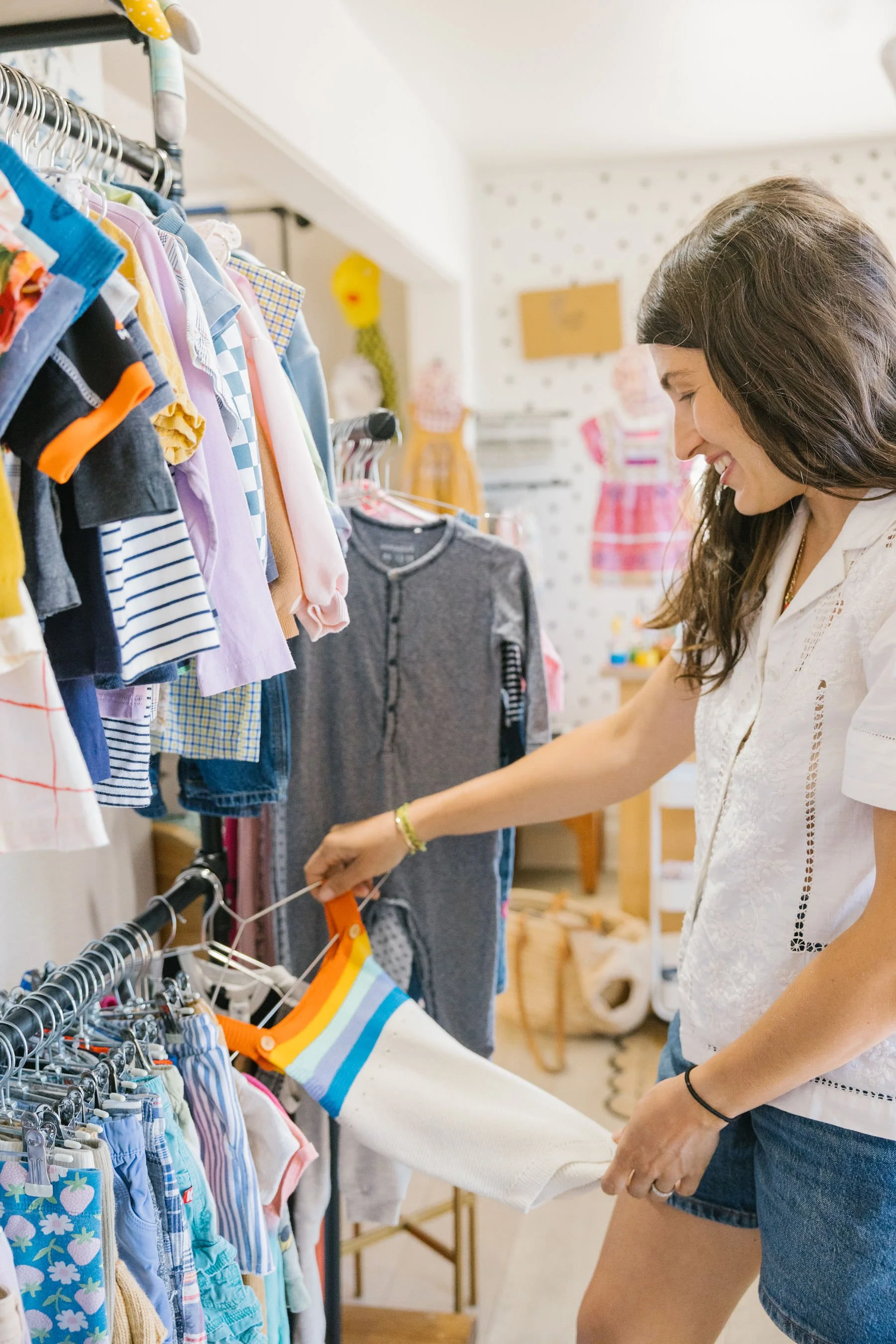 A woman shopping for clothes in a store, looking at children's clothing on a rack.