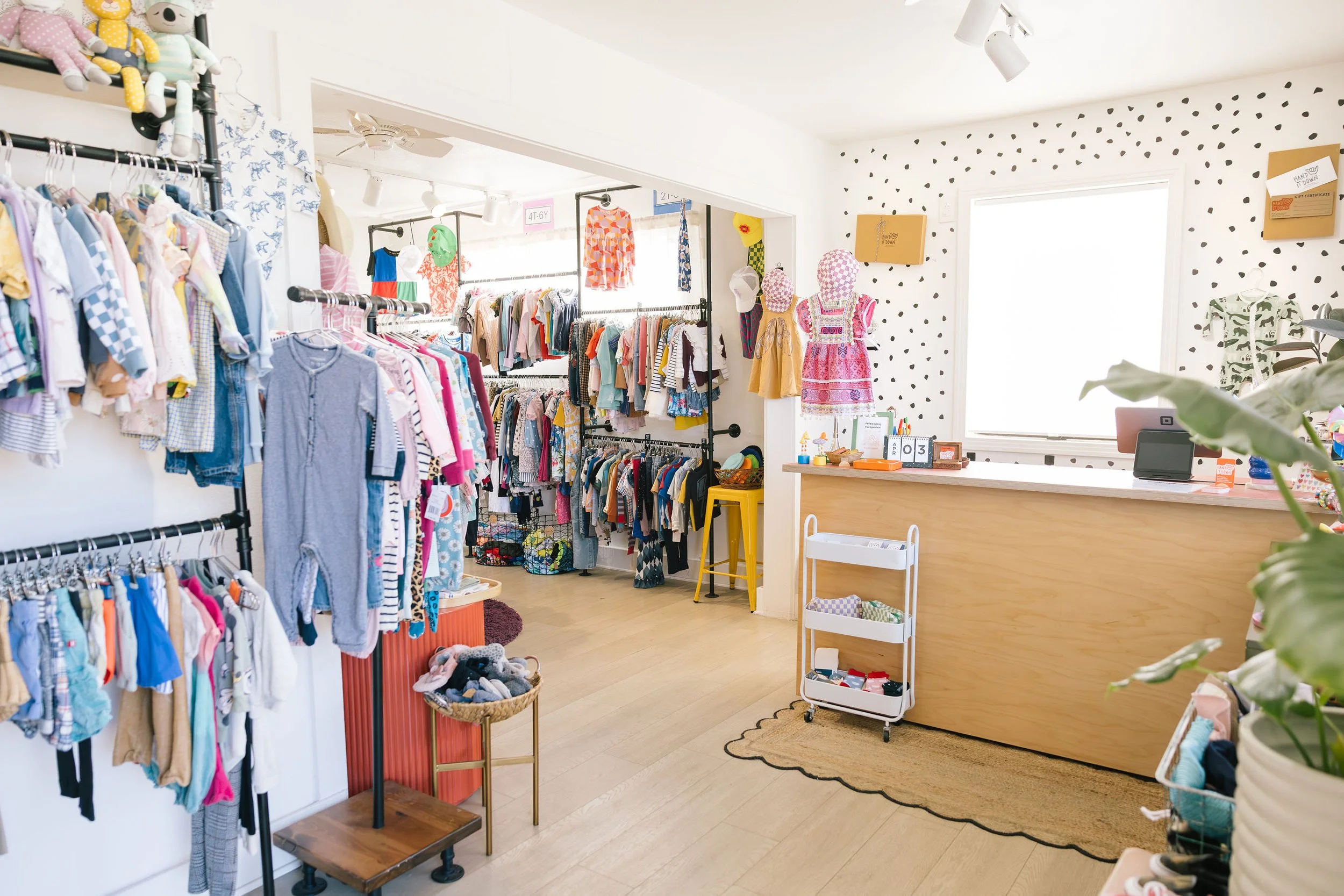 Hand It Down Santa Cruz, CA kid's clothing boutique with racks of colorful kids' clothes, toys, and accessories, and a checkout counter with a computer.