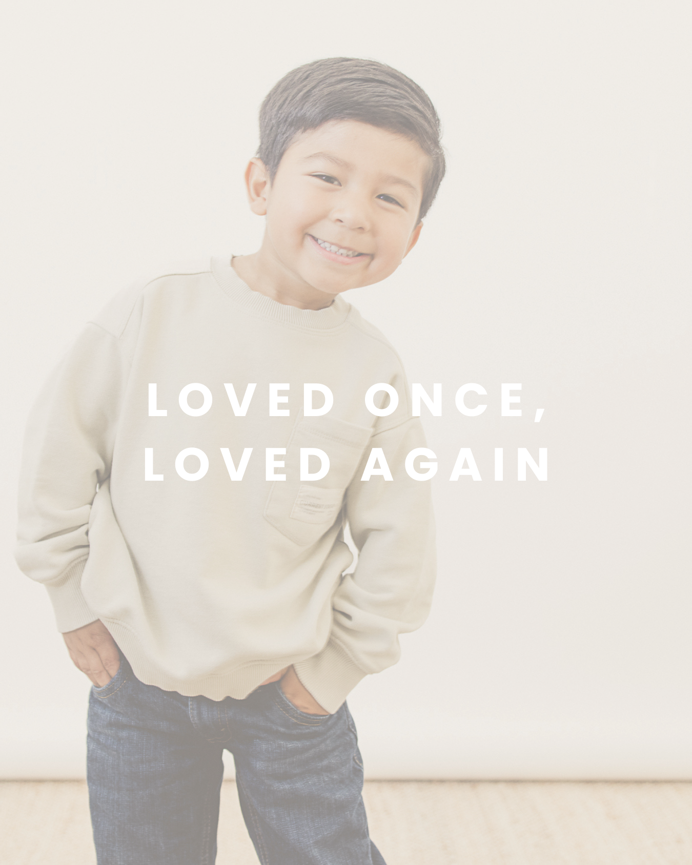 Young boy with short dark hair smiling, wearing a light beige sweatshirt and jeans, against a plain light-colored background, with the text "Loved Once, Loved Again" overlaid.