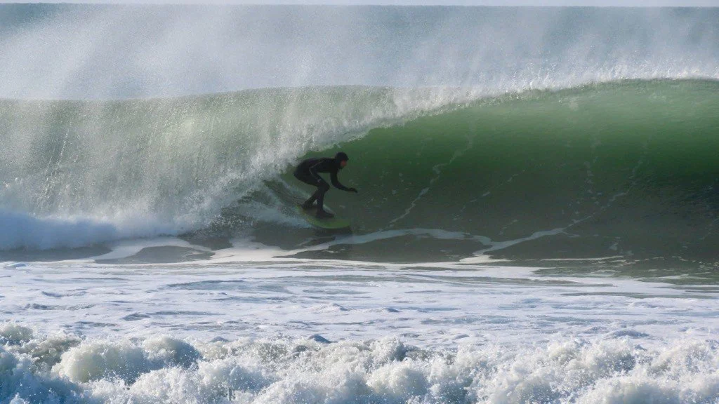 A person surfing inside a large green wave at the beach.