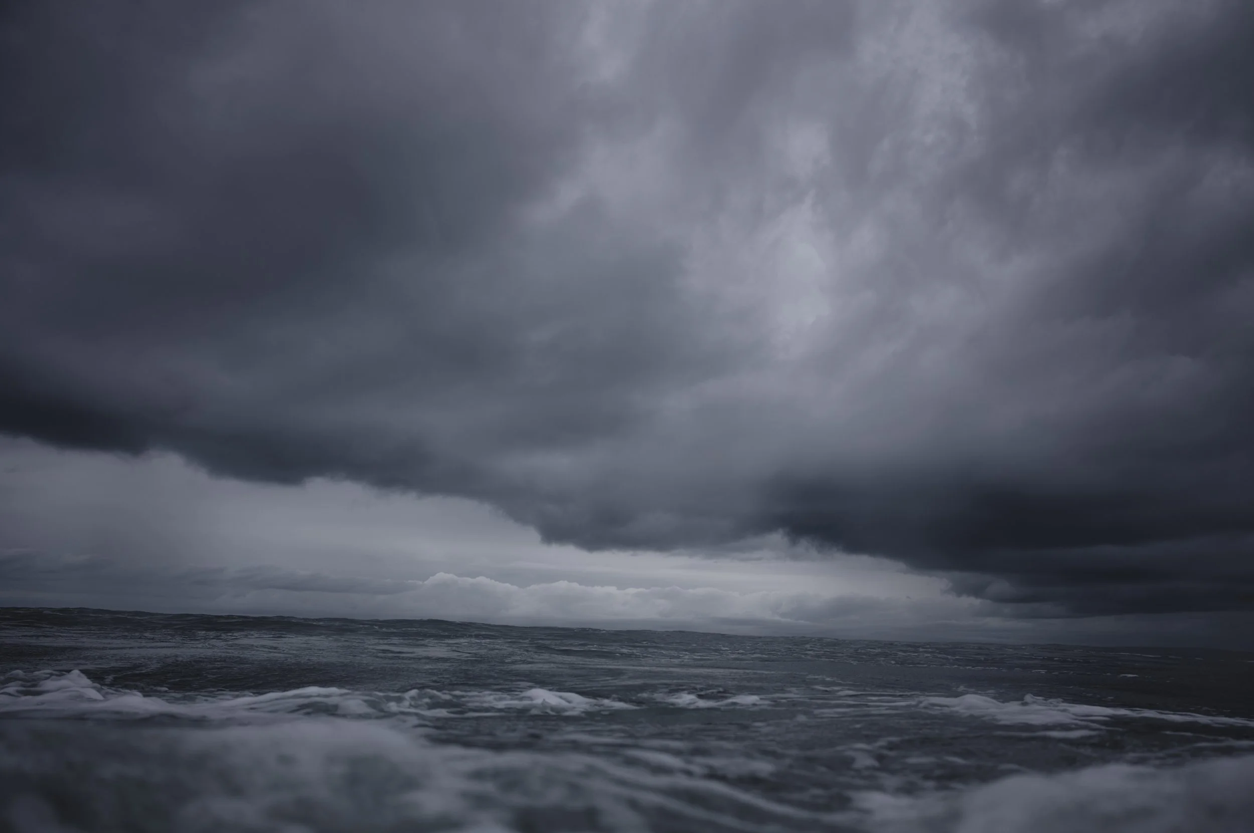 Dark storm clouds over the ocean, with waves crashing on the shore under a cloudy sky.