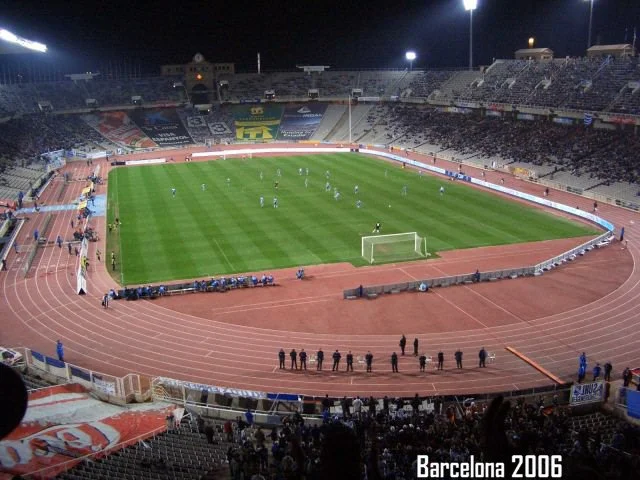 Fußballstadion in Barcelona im Jahr 2006, abends, mit Spielern auf dem Platz, Stadionbeleuchtung eingeschaltet, leere Sitze, Zuschauer im Hintergrund.