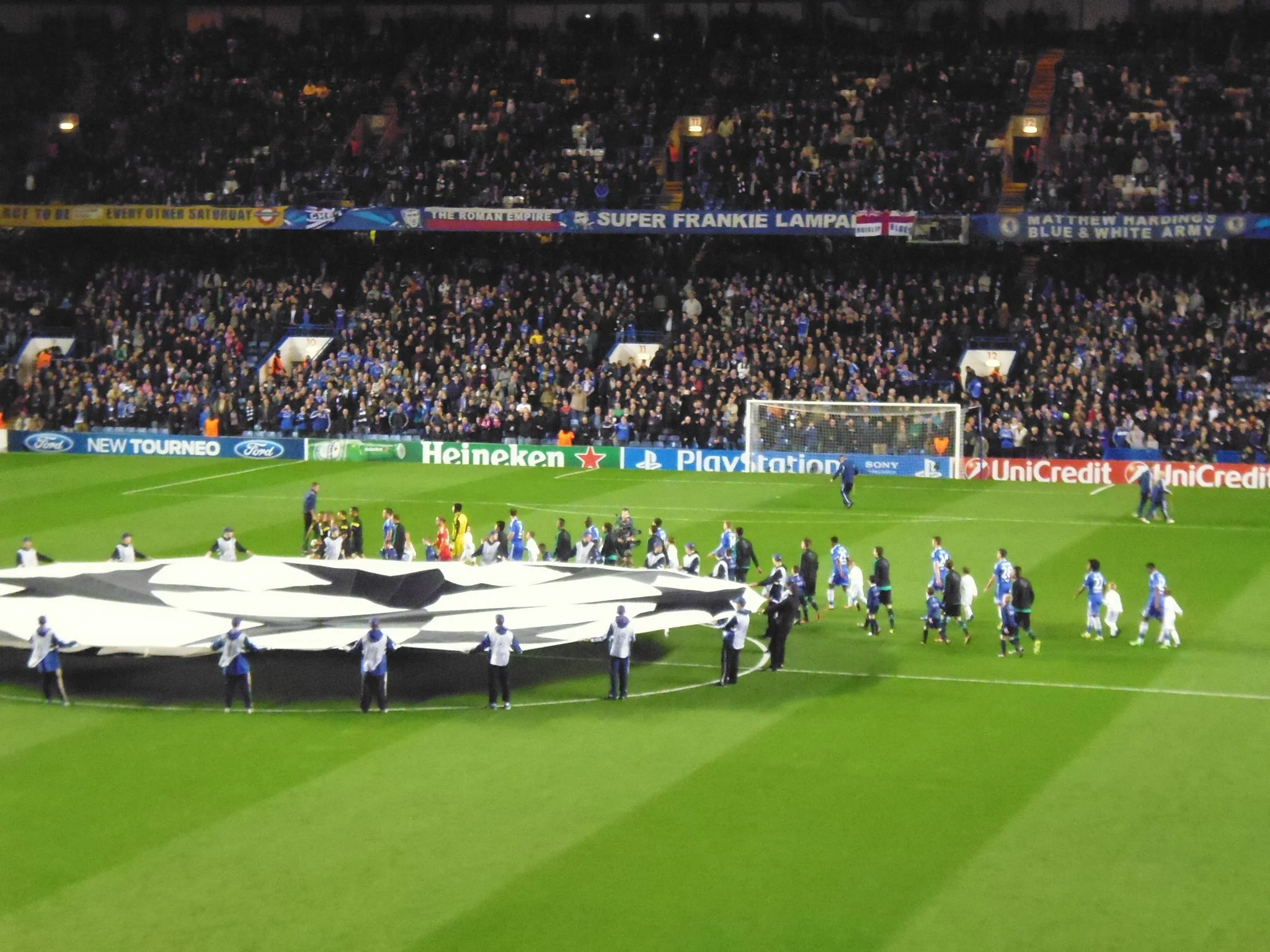 Fußballspiel in einem großen Stadion mit vielen Zuschauern, Flaggen und Werbung an der Bande.