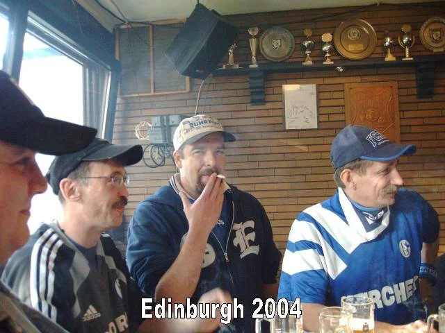 Vier Männer in Fußballtrikots, eine Bar, Holzverkleidung, Pokale und Trophäen an der Wand, männliche Gesichter, eine Gruppe von Fußballfans in Edinburgh 2004.