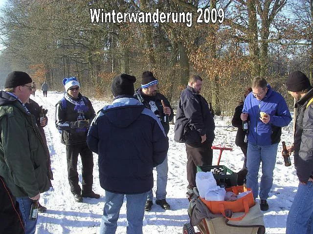 Gruppe von Menschen beim Winterwandern 2009, einige trinken und essen in schneebedecktem Wald.
