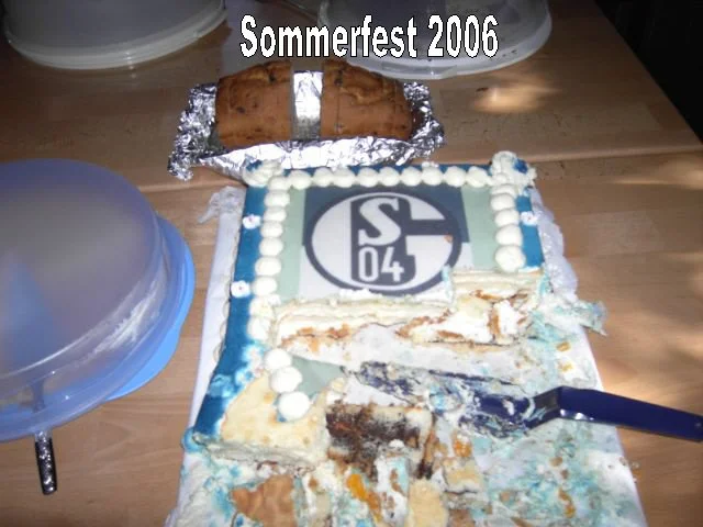 Schneide eines halb verfressenen Geburtstagskuchens mit dem Logo des FC Schalke 04, im Hintergrund zwei Kuchenstücke auf Alufolie, oben die Aufschrift 'Sommerfest 2006'.