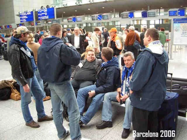 Gruppe von Menschen sitzt und steht in einem Flughafen, mit Check-in-Schaltern im Hintergrund, im Jahr 2006 in Barcelona.