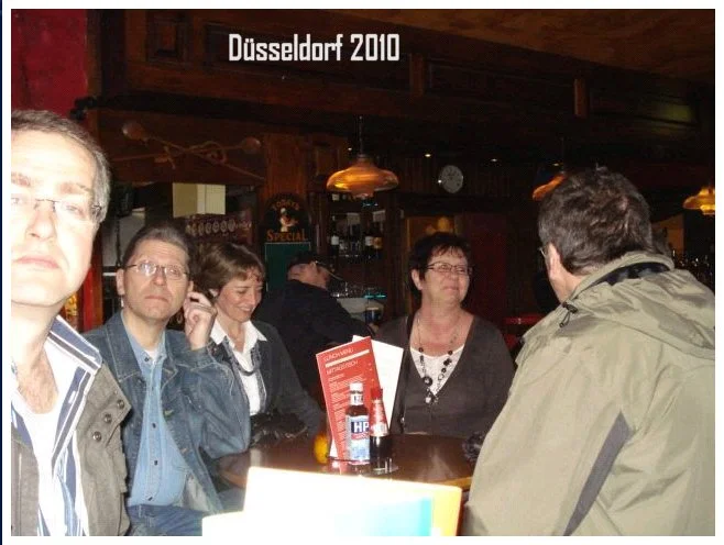 Menschen sitzen an einem Tisch in einer Bar oder einem Pub in Düsseldorf im Jahr 2010, einige sprechen mit dem Mann im Vordergrund, der von hinten zu sehen ist.