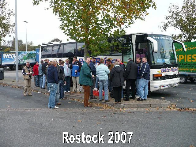 Menschen stehen in einer Schlange vor einem Bus im Außenbereich, im Hintergrund Bäume und Werbetafeln, es ist herbstlich, Rostock 2007.
