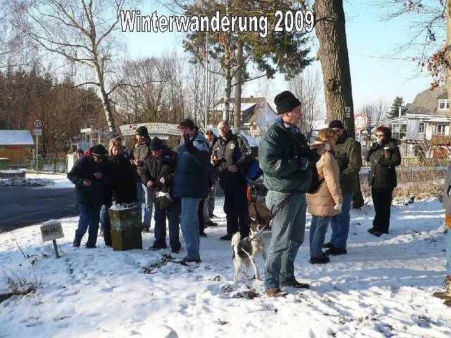 Gruppe von Menschen bei einer Winterwanderung im Jahr 2009, Schneelandschaft, einige mit Hunden, im Hintergrund Bäume und Häuser