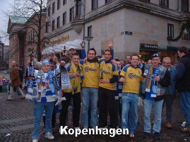 Gruppe von Menschen in Kopenhagener Stadtmitte, einige tragen Schal und Trikots des FC Kopenhagen, feiern mit Getränken, im Hintergrund Gebäude mit Geschäften.