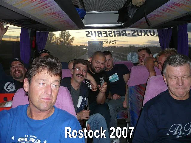 Gruppe von Menschen sitzend auf einem Bus, einige lachen, während der Sonnenuntergang im Hintergrund sichtbar ist. Bild ist von der Reise in Rostock im Jahr 2007.