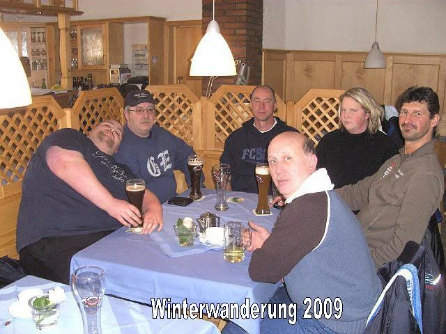 Sechs Menschen sitzen um einen Tisch in einer Gaststätte, einige mit Getränken. Es scheint eine Gruppentour im Winter zu sein, aufgenommen im Jahr 2009.