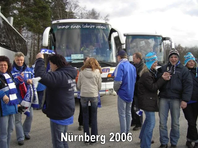 Gruppe von Menschen im Café vor einem Bus, Nürnberg 2006, viele tragen blaue Kleidung und Wintermützen, einige machen Fotos.